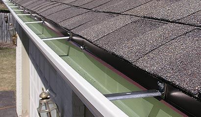 Roof gutter with green leaf guard along a gray shingled roofline