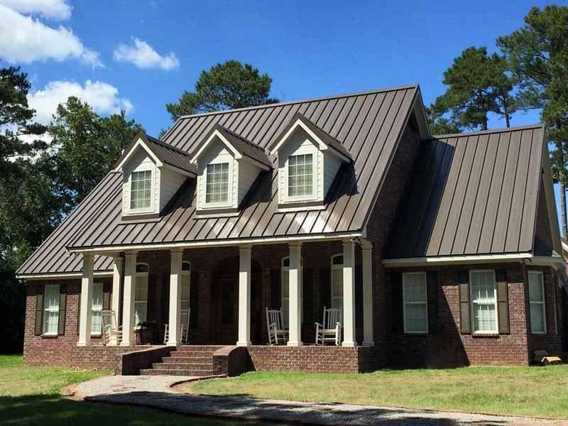 Brick house with brown metal roof and three dormer windows under a blue sky
