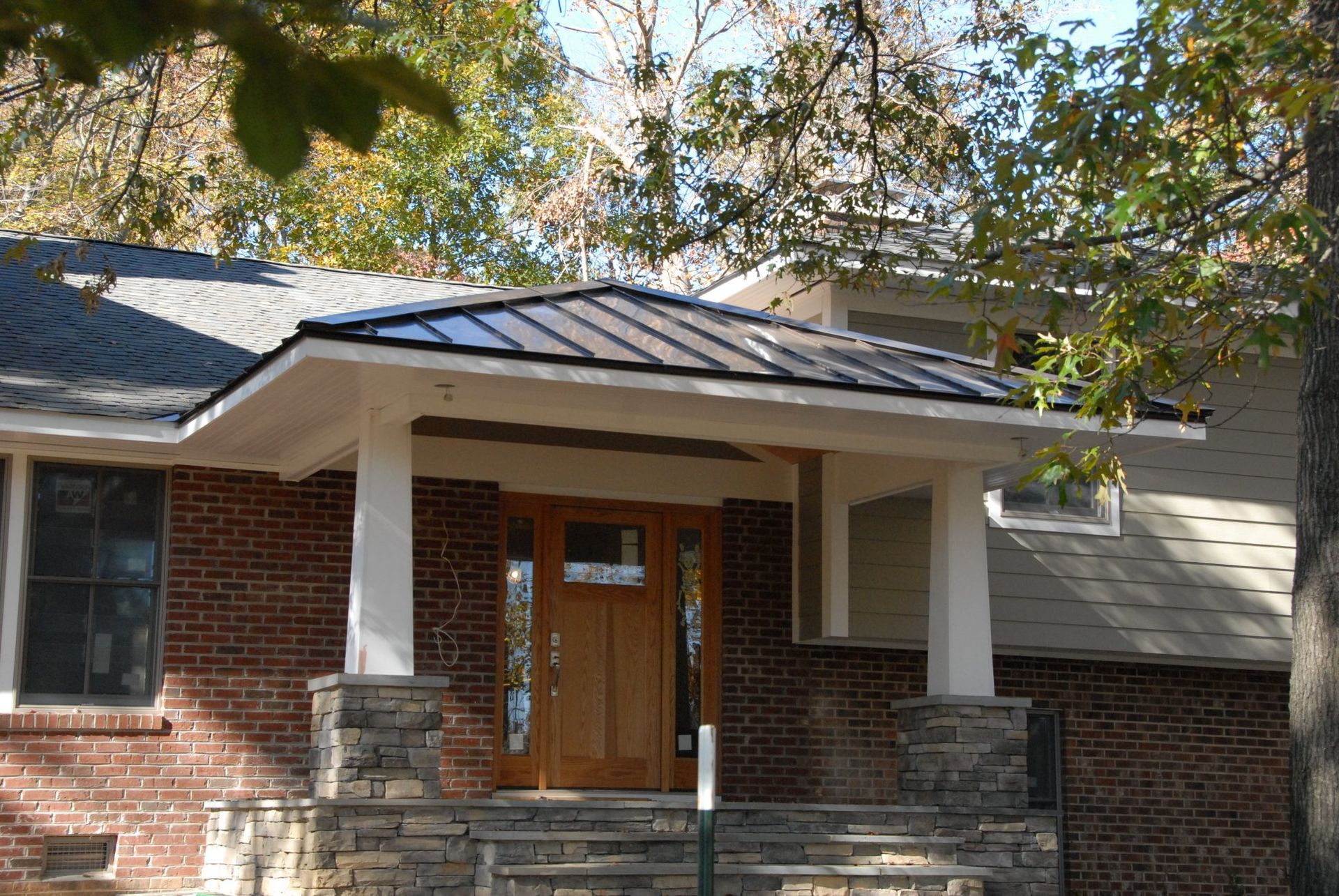 Brick house front entrance with wooden door, covered porch, and stone steps under trees
