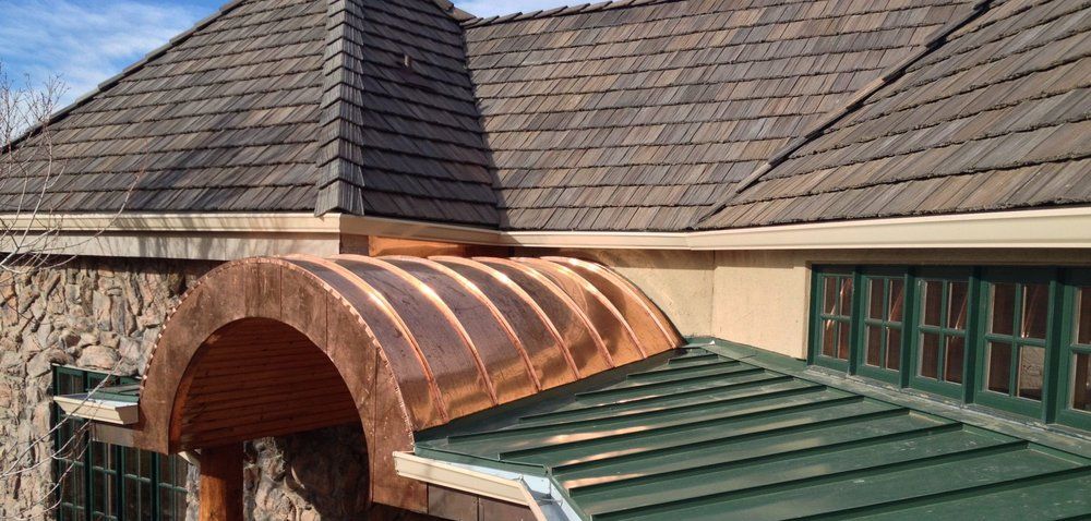 Copper-roofed arched entrance beside a green metal roof on a stone building
