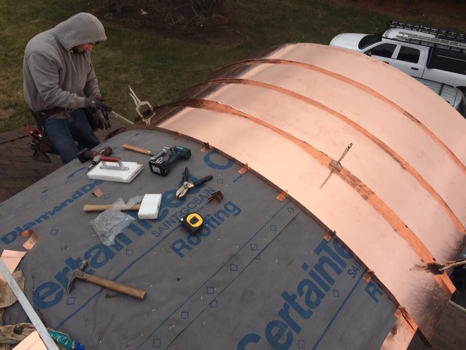Worker roofing a curved copper dome with tools on top of a building
