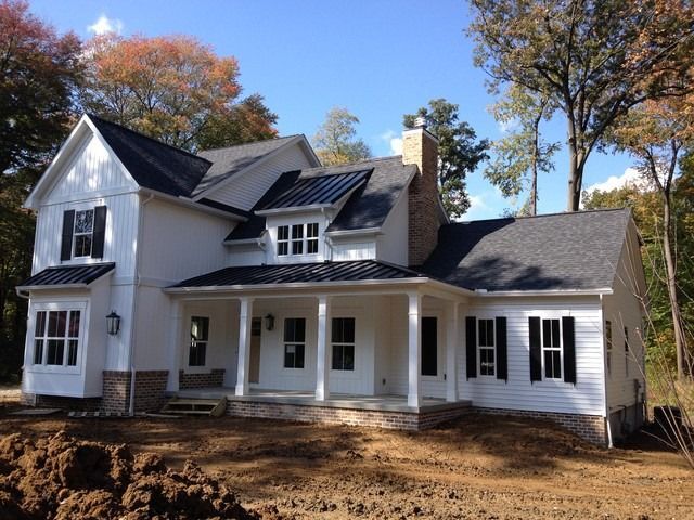 White two-story farmhouse with black roof and porch, set among autumn trees.
