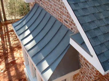 Curved gray metal roof beside a brick house and dark shingle roof, viewed from above