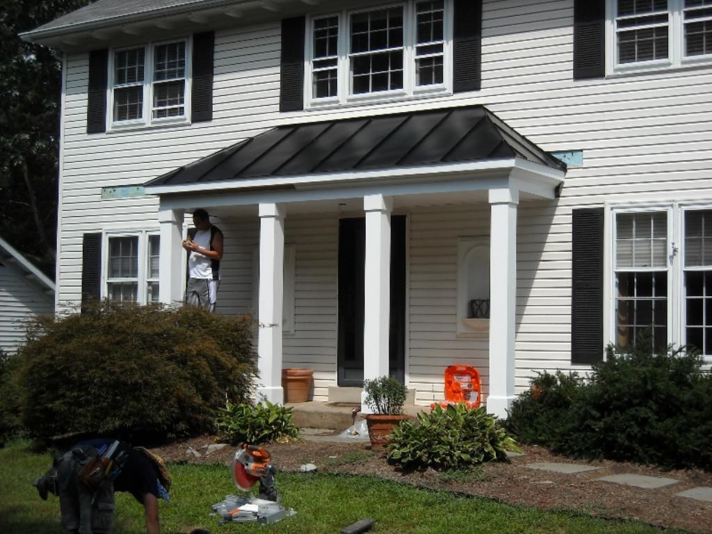 Person on a porch of a white house, with two dogs in the front yard and Halloween decorations near the steps