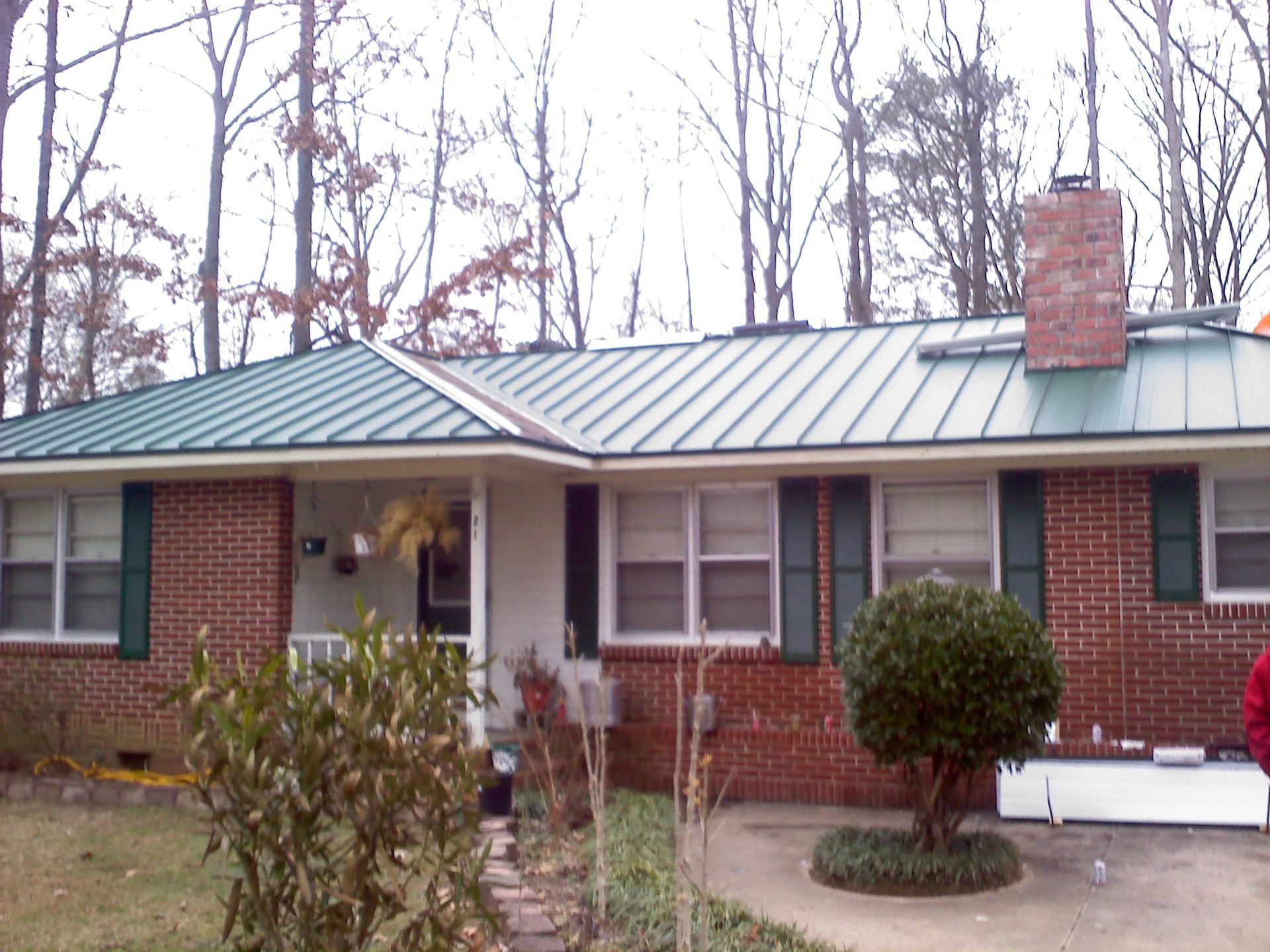 Brick ranch house with green metal roof, front porch, and bare trees in the yard