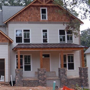 Two-story house with gray siding, stone porch columns, and unfinished wood trim