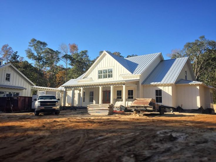 New house under construction with white siding and metal roof, truck and lumber in front yard