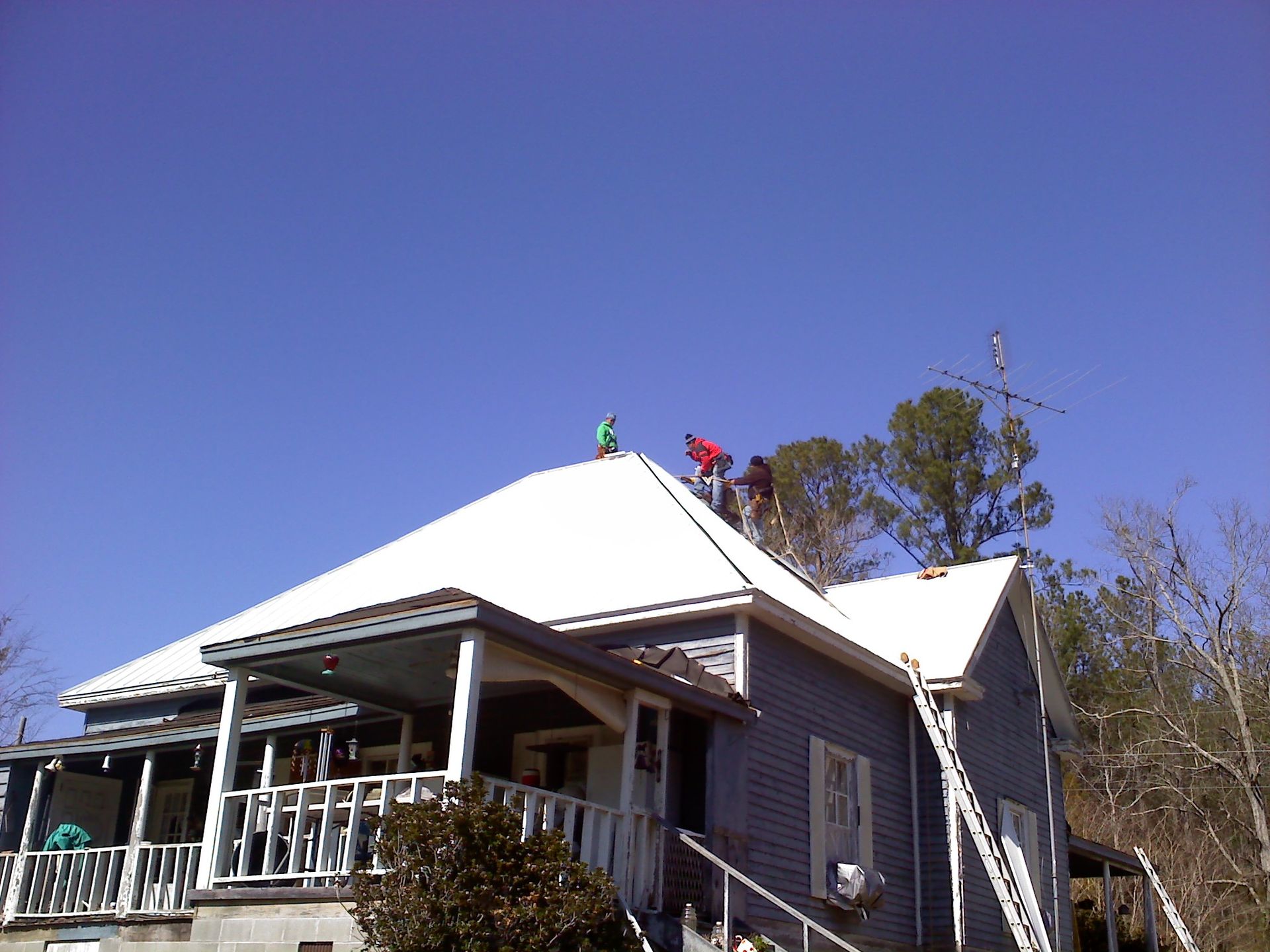 Two workers on a house roof under construction, with a white roof and blue sky.