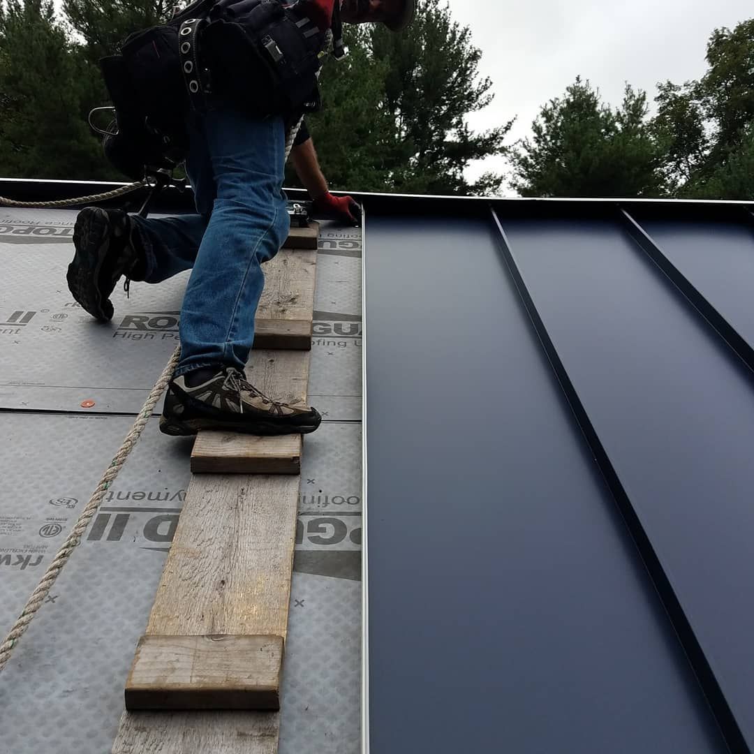 Worker standing on a wooden plank on a roof beside a dark metal roof panel