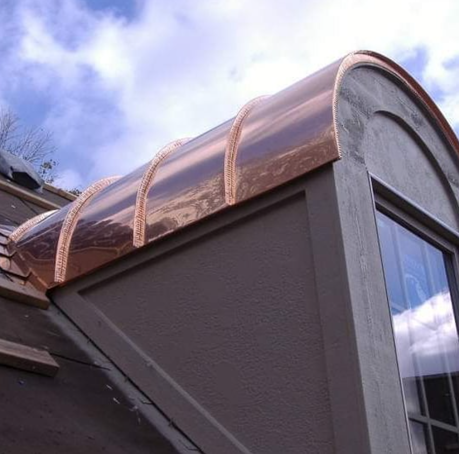 Copper-clad curved roof with arched supports on a modern building against a cloudy sky