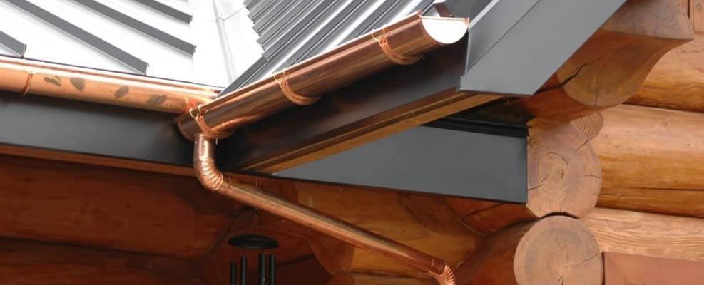 Wooden roof eaves with copper gutter and downspout on a house exterior