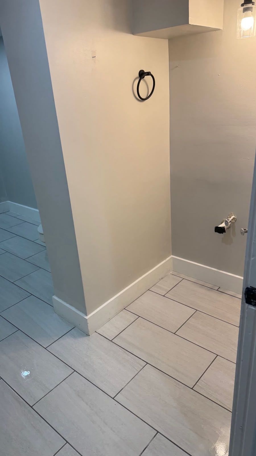 Small tiled room with white walls, a floor drain, and exposed wall fixtures, likely a bathroom under renovation