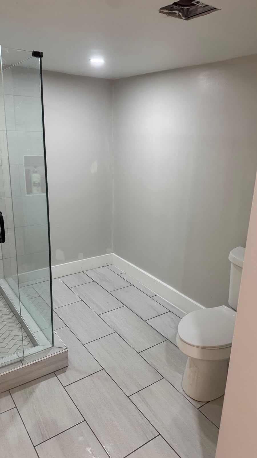 Small bathroom with glass shower, white tiled floor, and toilet against a gray wall.
