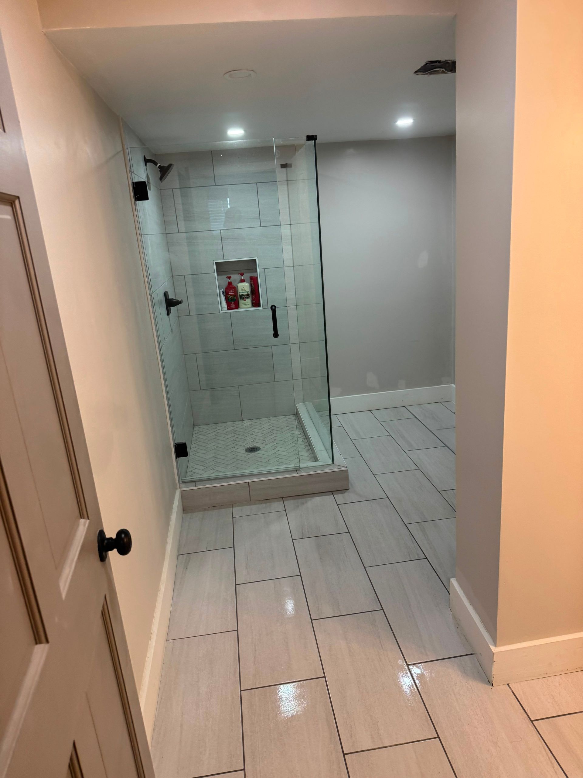 Bathroom with white tile floor, glass shower enclosure, and recessed ceiling lights.