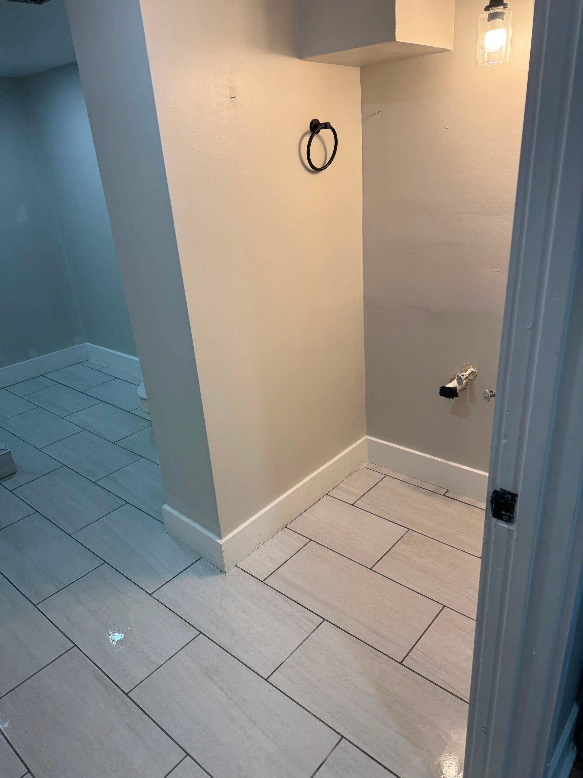 Small tiled bathroom with a shower area, beige walls, and white floor tiles seen through an open door