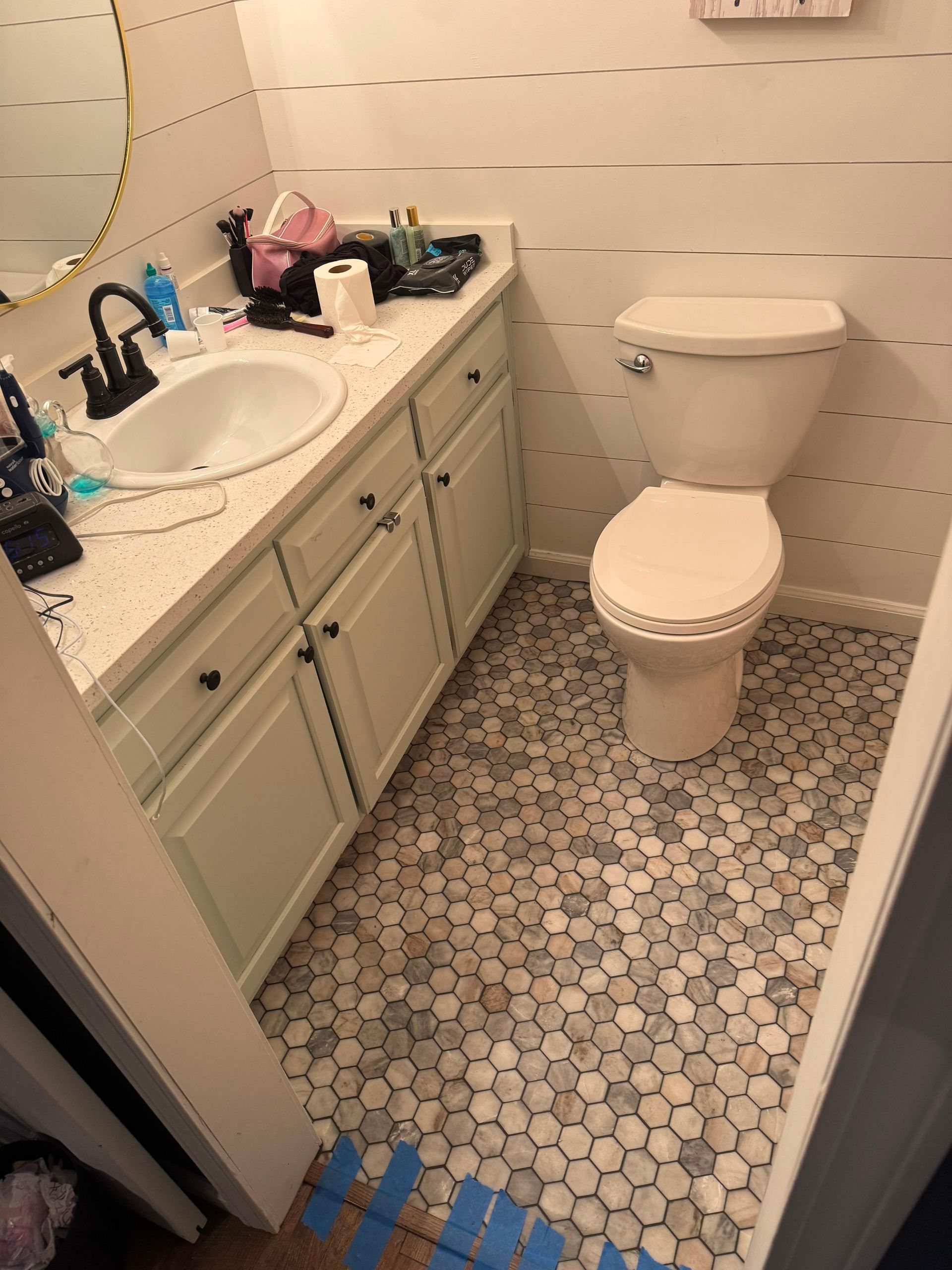 Small bathroom with white toilet, beige vanity, and hexagon tile floor.