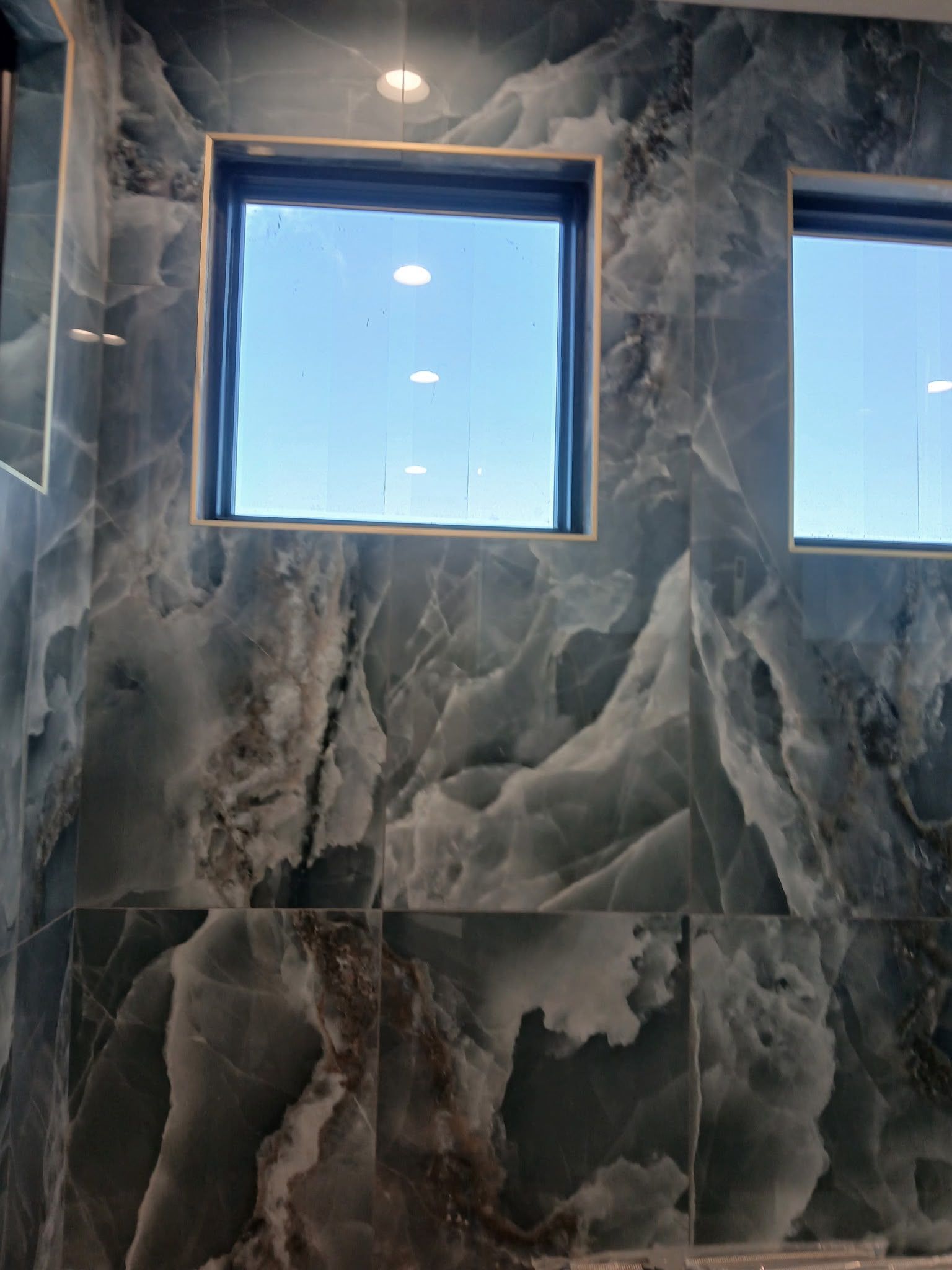 Gray marble-tiled wall with two square windows in a bright bathroom or shower area