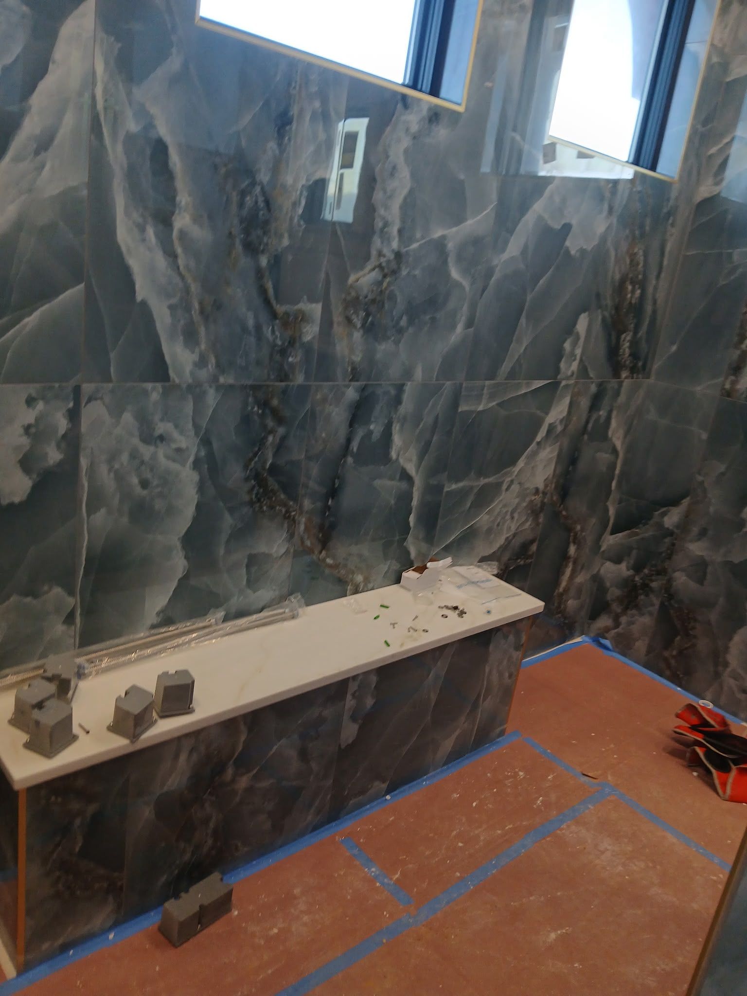 Large marble-tiled wall with a narrow shelf and small figurines over an orange floor marked with blue tape in a bright room