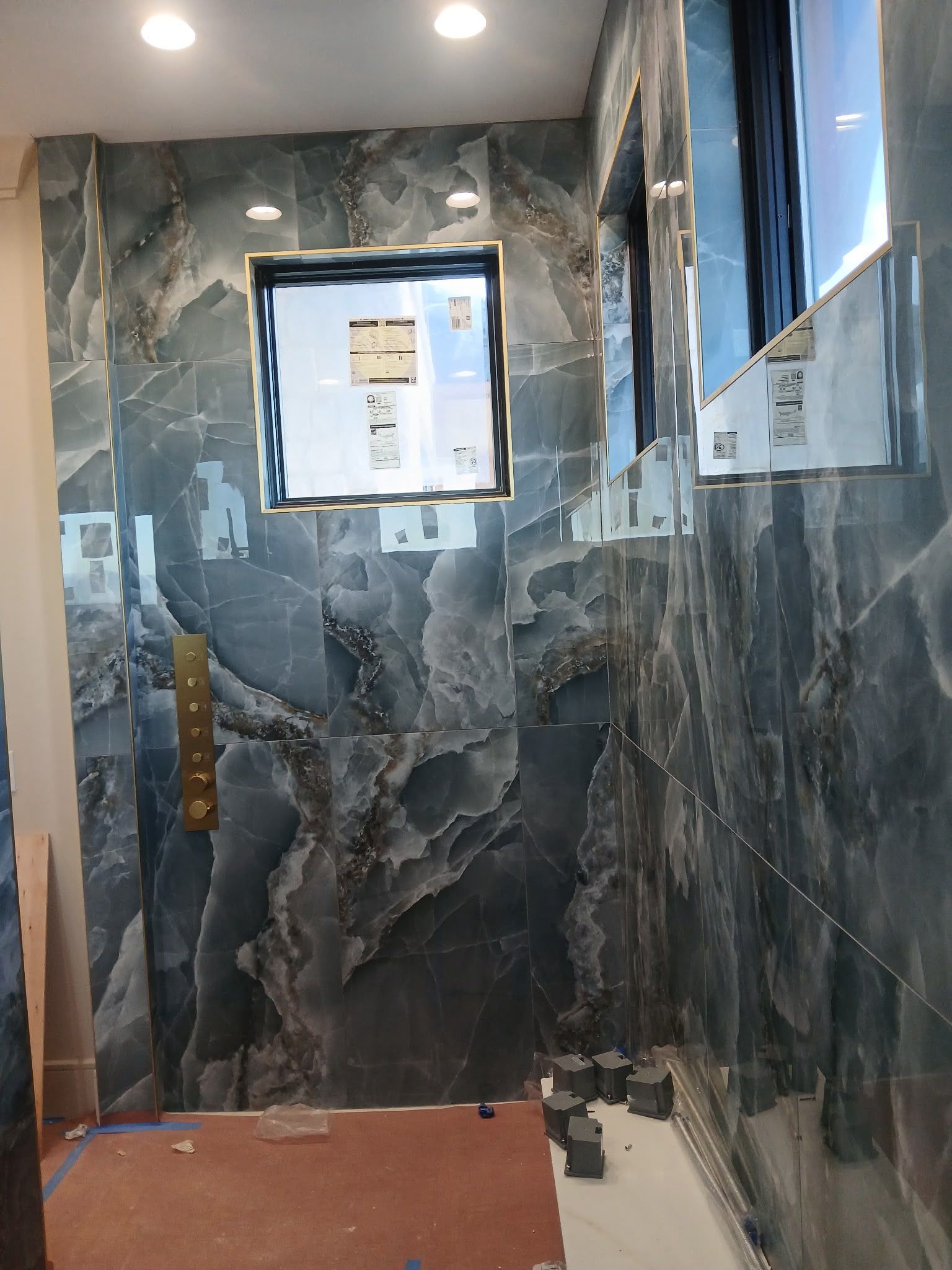 Narrow bathroom with dark marble tile, a window, shower fixtures, and a bare floor under construction