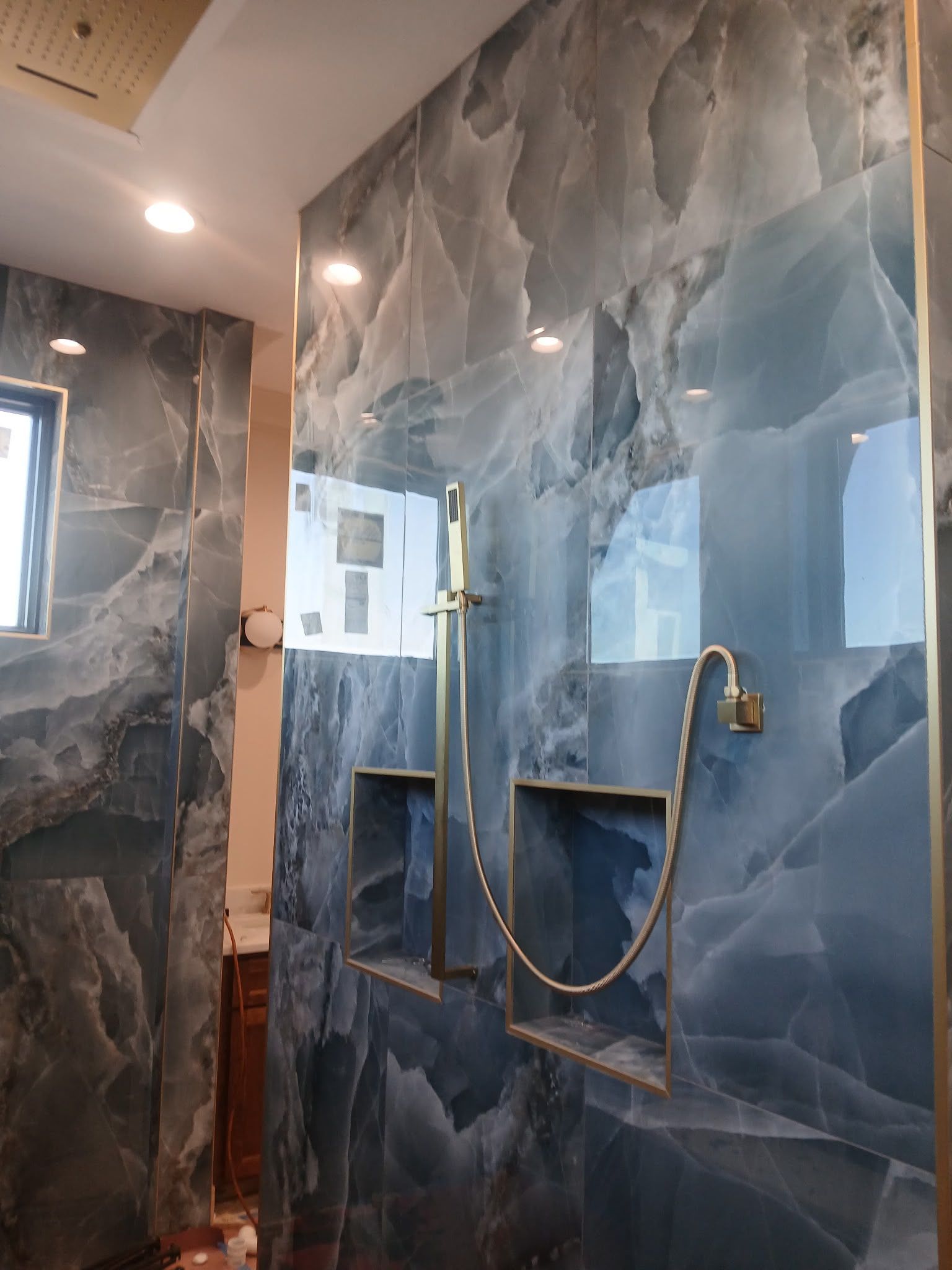 Modern bathroom shower with blue-gray marble tile, glass door, and brass fixtures