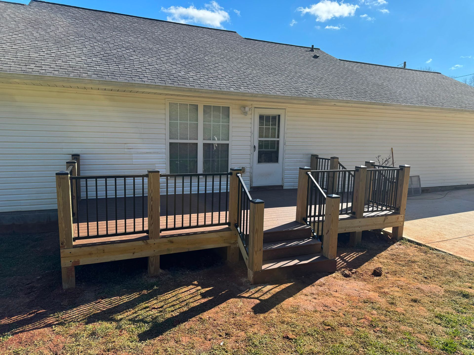 White house with small wooden front deck and steps under a blue sky.