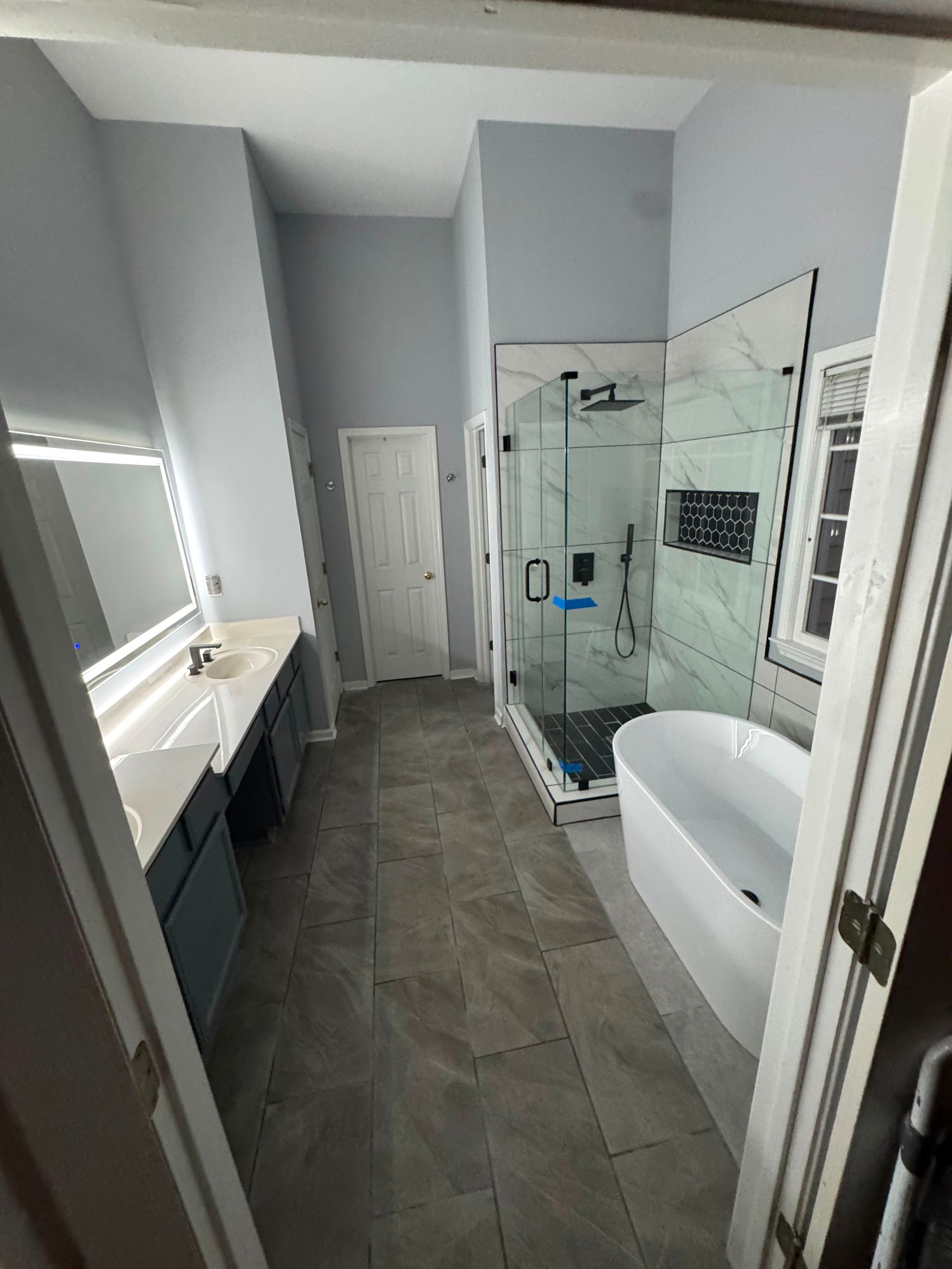 Modern bathroom with glass shower, vanity, and white bathtub on gray tile floor