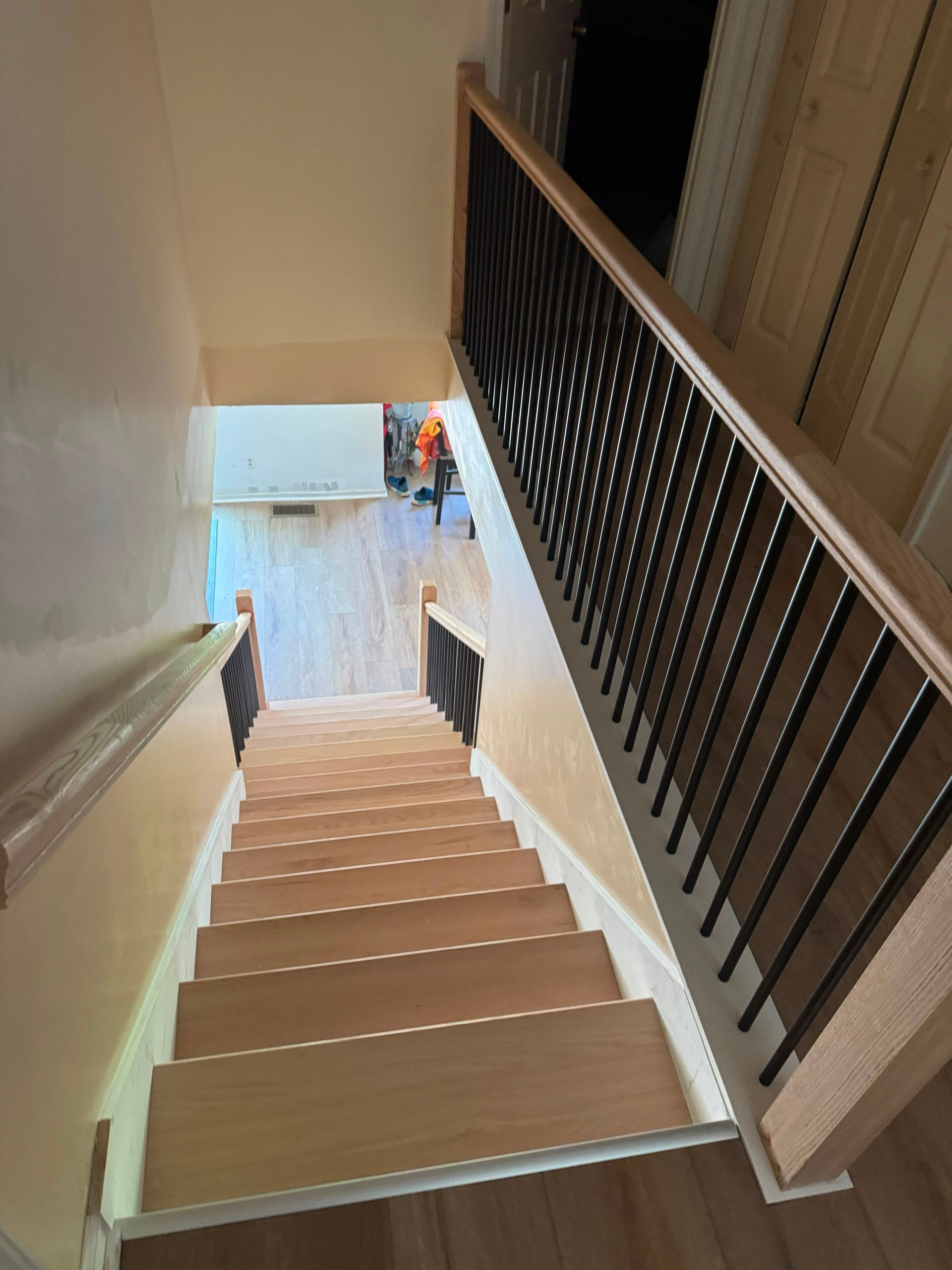 Top-down view of a carpeted staircase with black railing, leading to a bright entryway below.