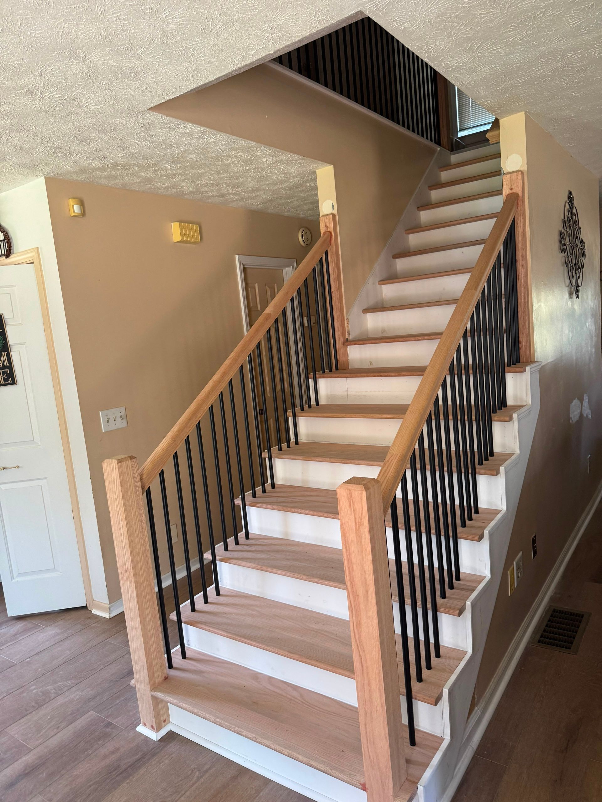 Interior staircase with beige carpet, wood handrails, and black balusters in a home entryway