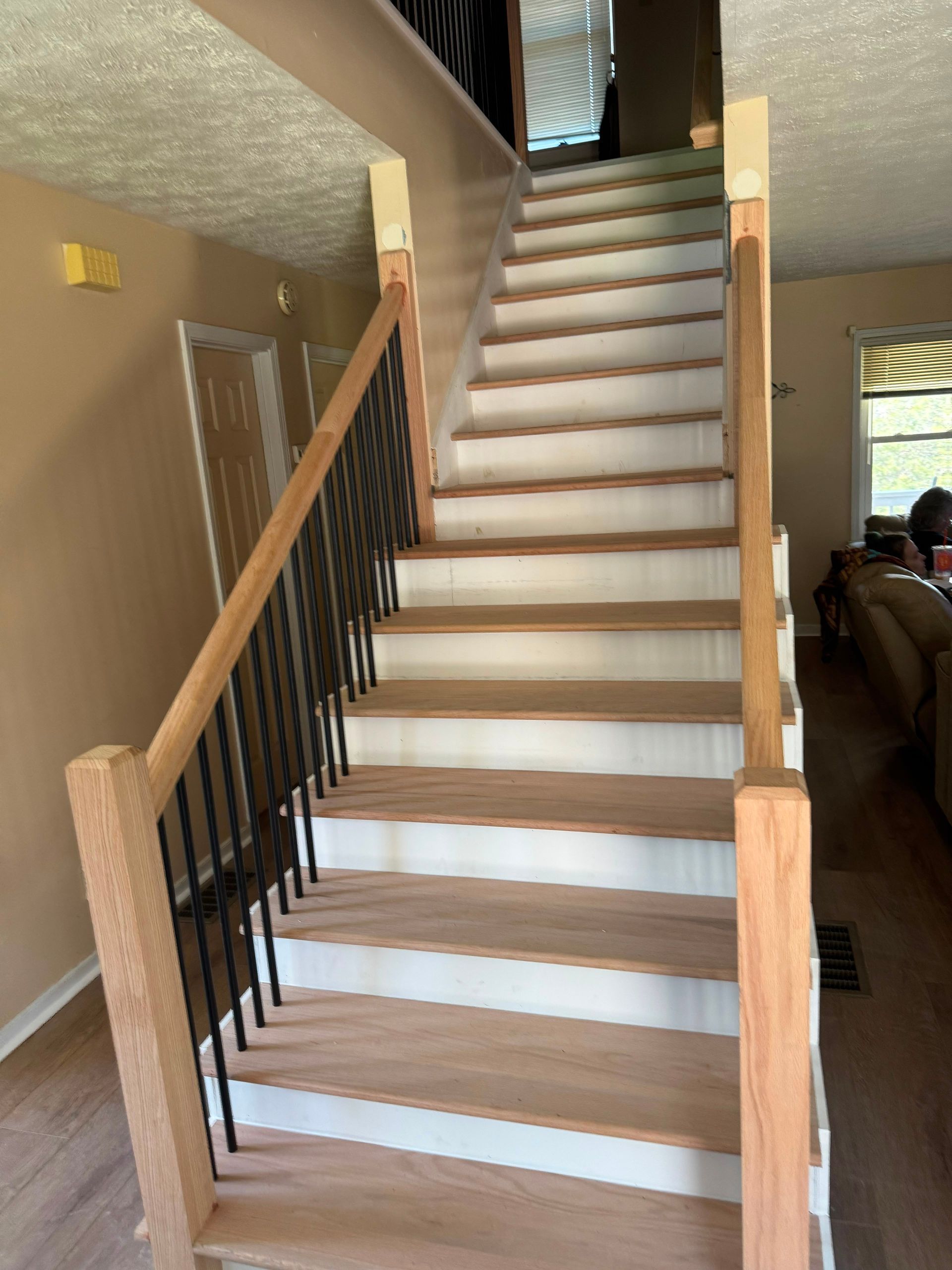 Indoor staircase with beige carpet, light wood railing, and black balusters in a home interior