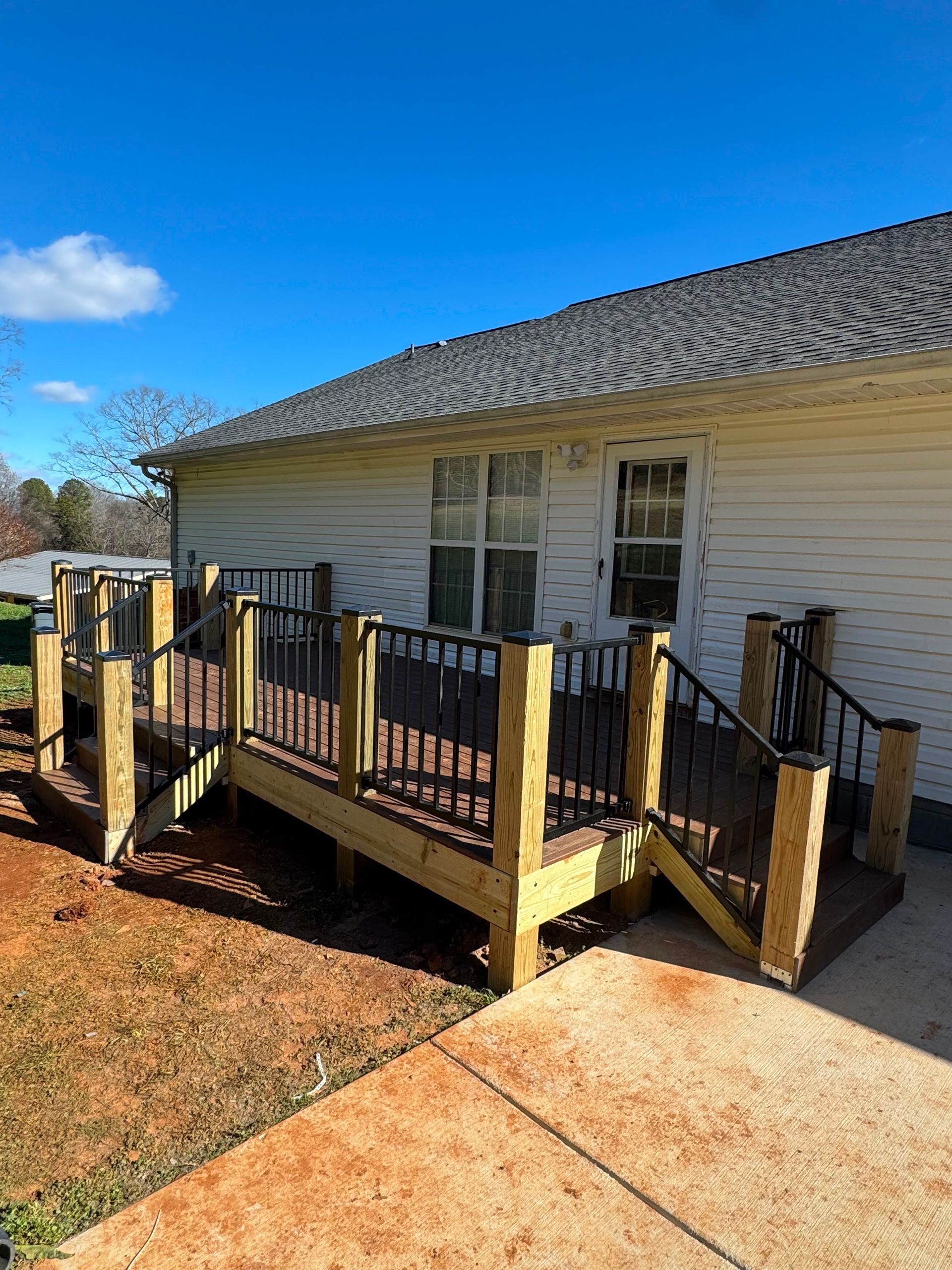 Wooden wheelchair ramp and steps leading to a white house with a gray shingled roof on a sunny day