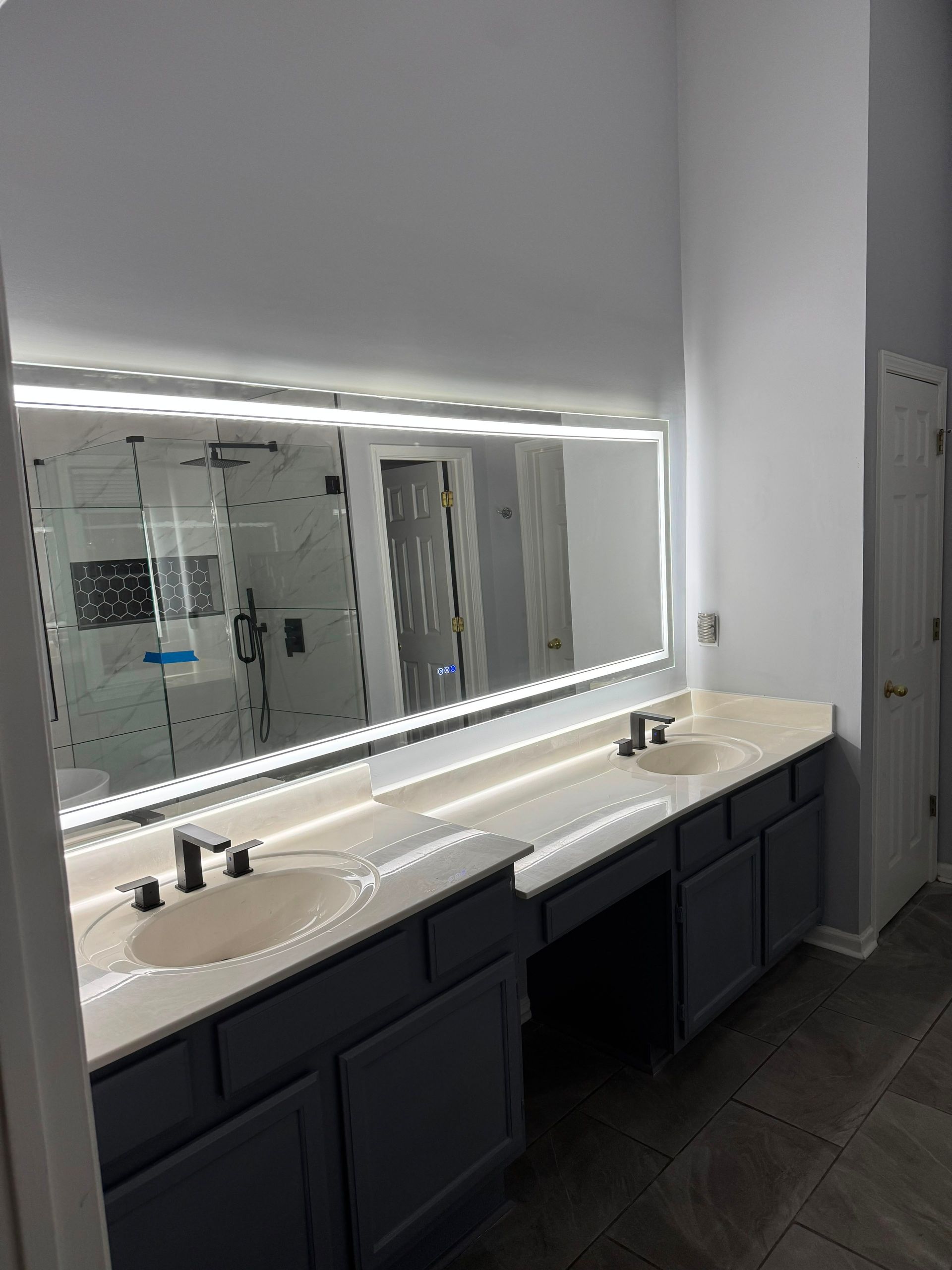 Modern bathroom vanity with large mirror, double sinks, and dark cabinets under bright lighting