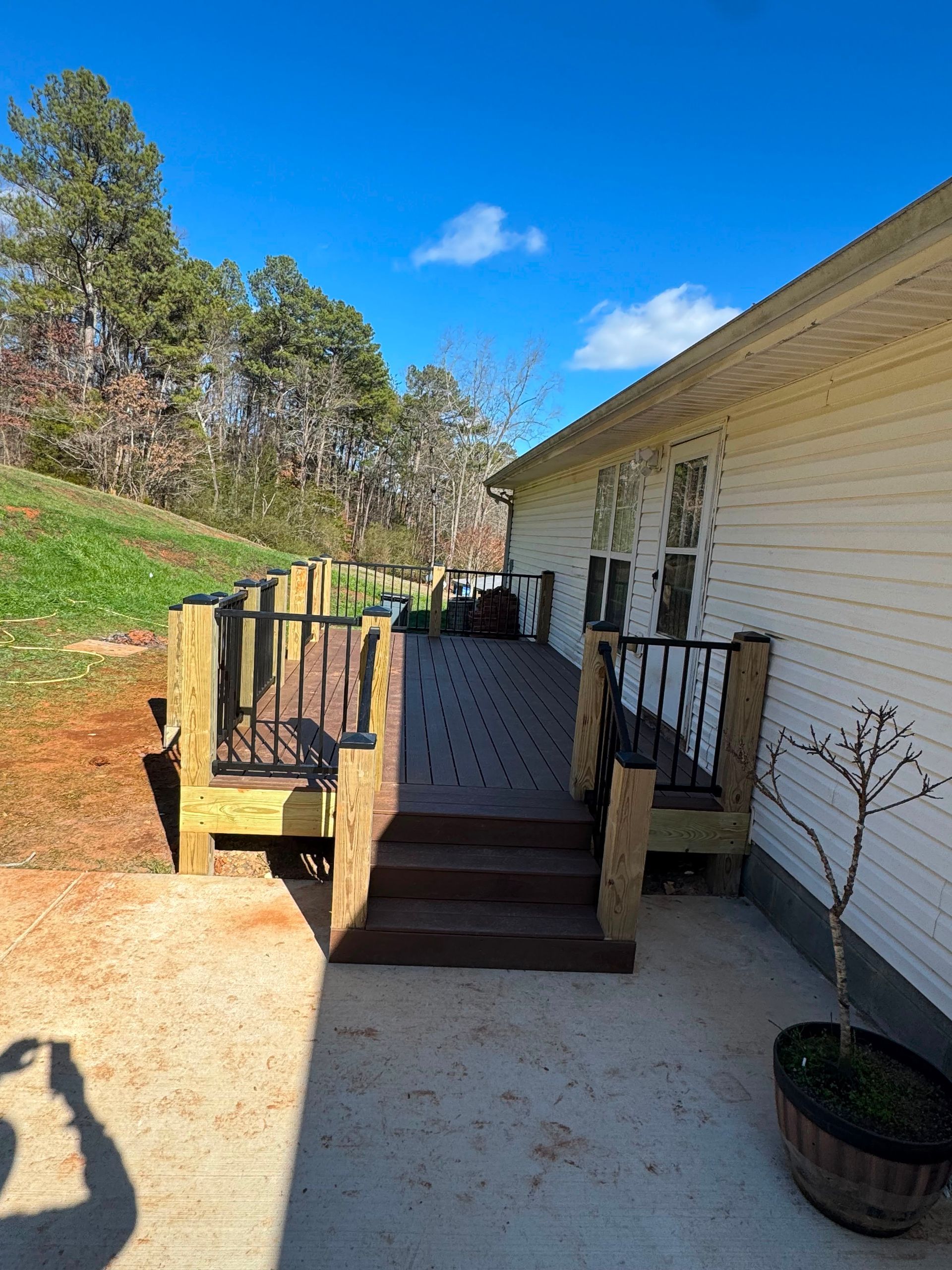 Front porch with steps, black railings, white siding, and a potted plant beside a sunny yard.