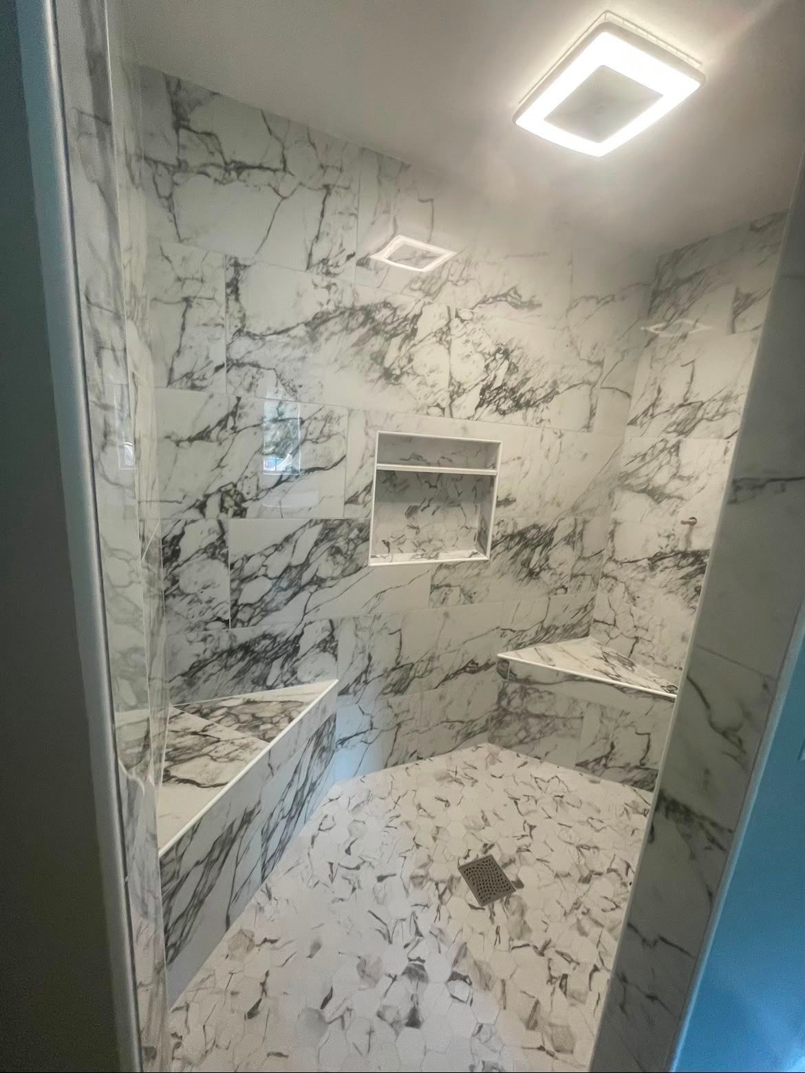 Marble-tiled shower with bench, recessed shelf, and overhead light