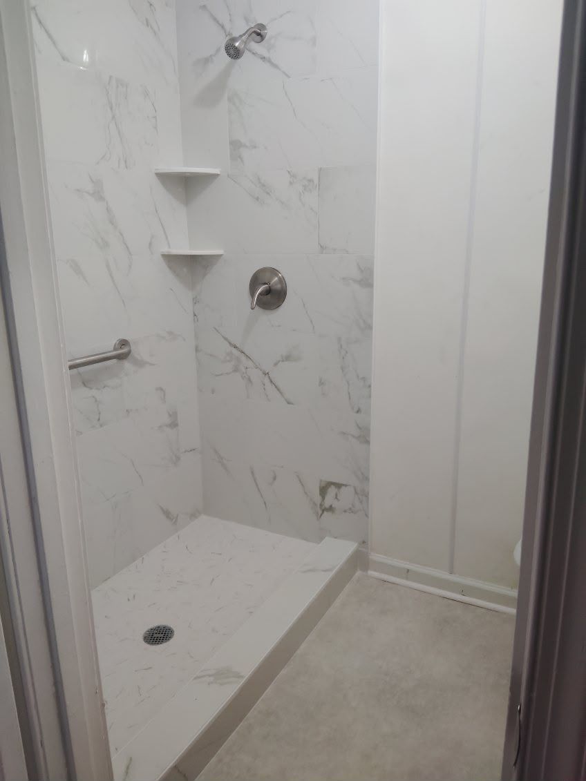 Modern walk-in shower with white marble-look tile, handheld shower, and built-in corner shelves