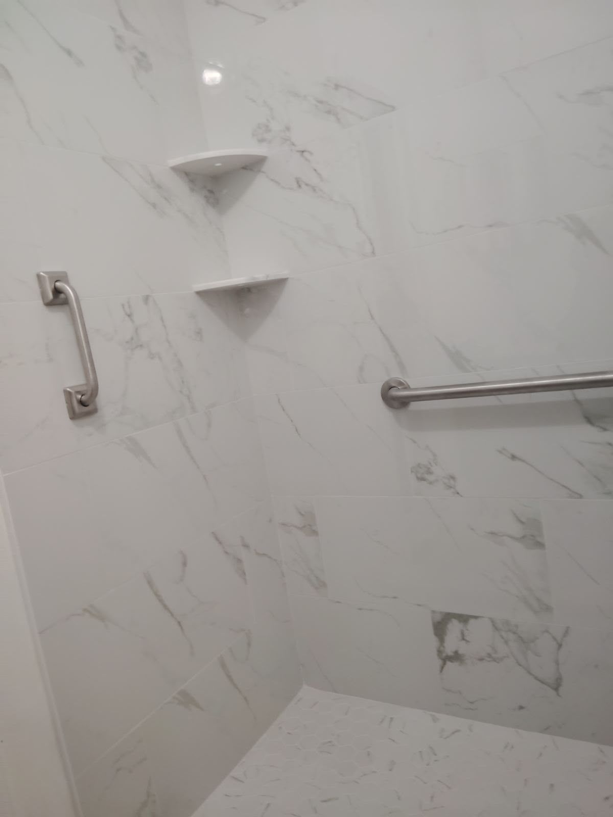 White tiled shower with corner shelves, grab bar, and bench seat
