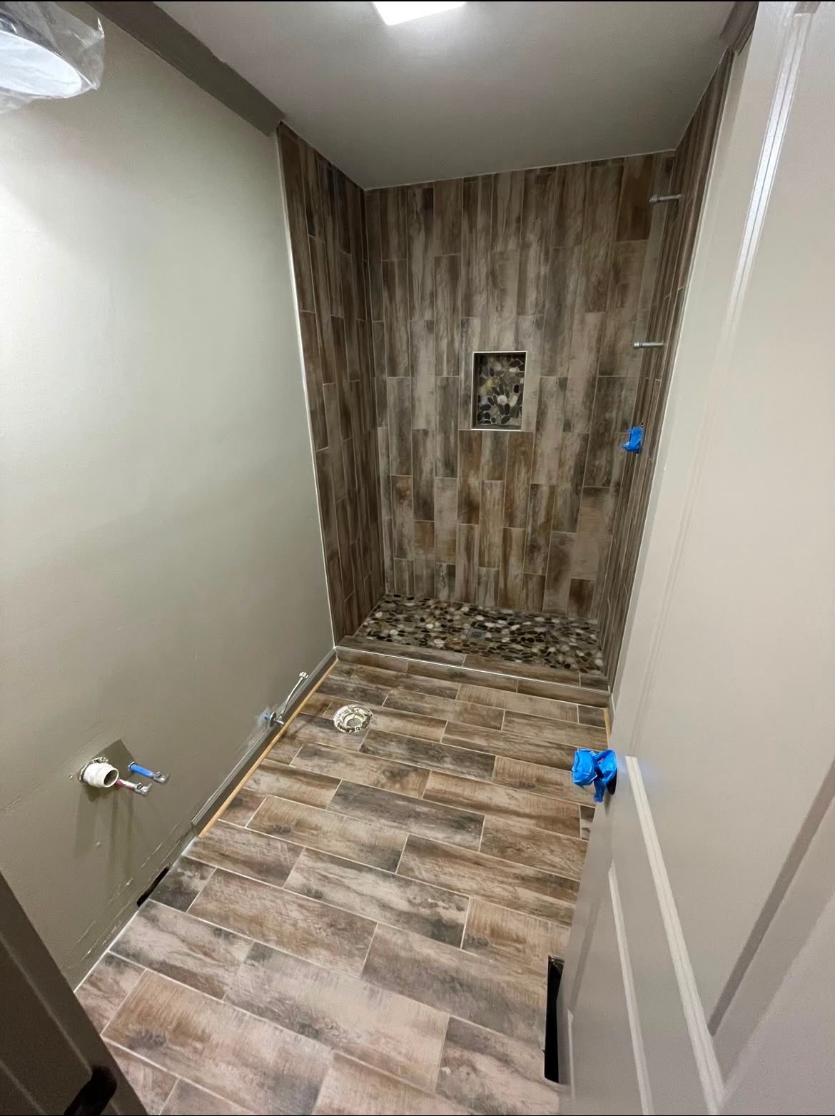 Small bathroom under renovation with wood-look tile walls and floor, toilet and shower fixtures visible.