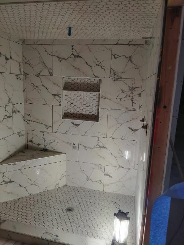 Tiled bathroom shower with built-in bench, small mirror niche, and a lantern on the floor