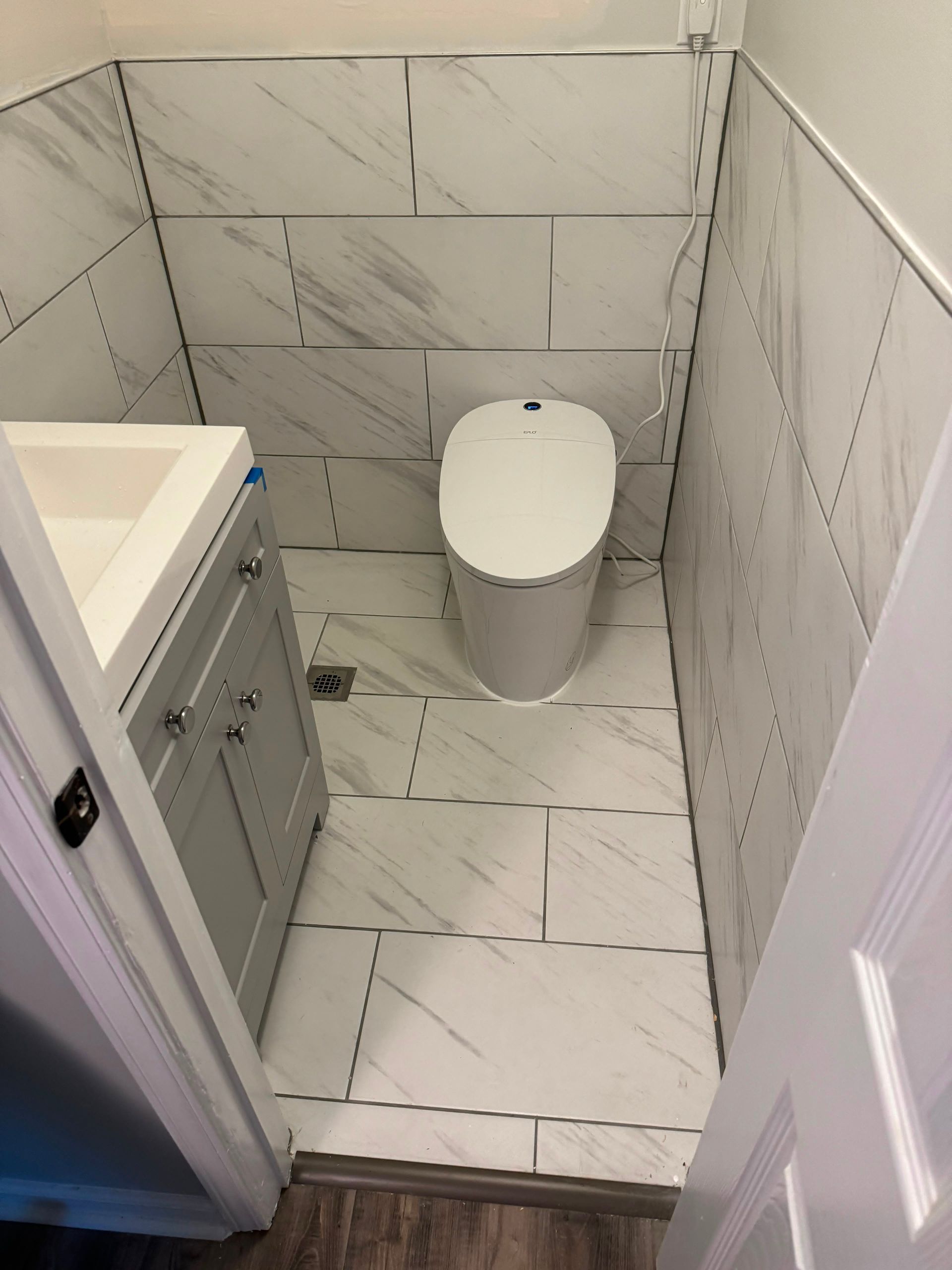 Small tiled bathroom with a toilet, sink vanity, and white marble-look walls and floor.