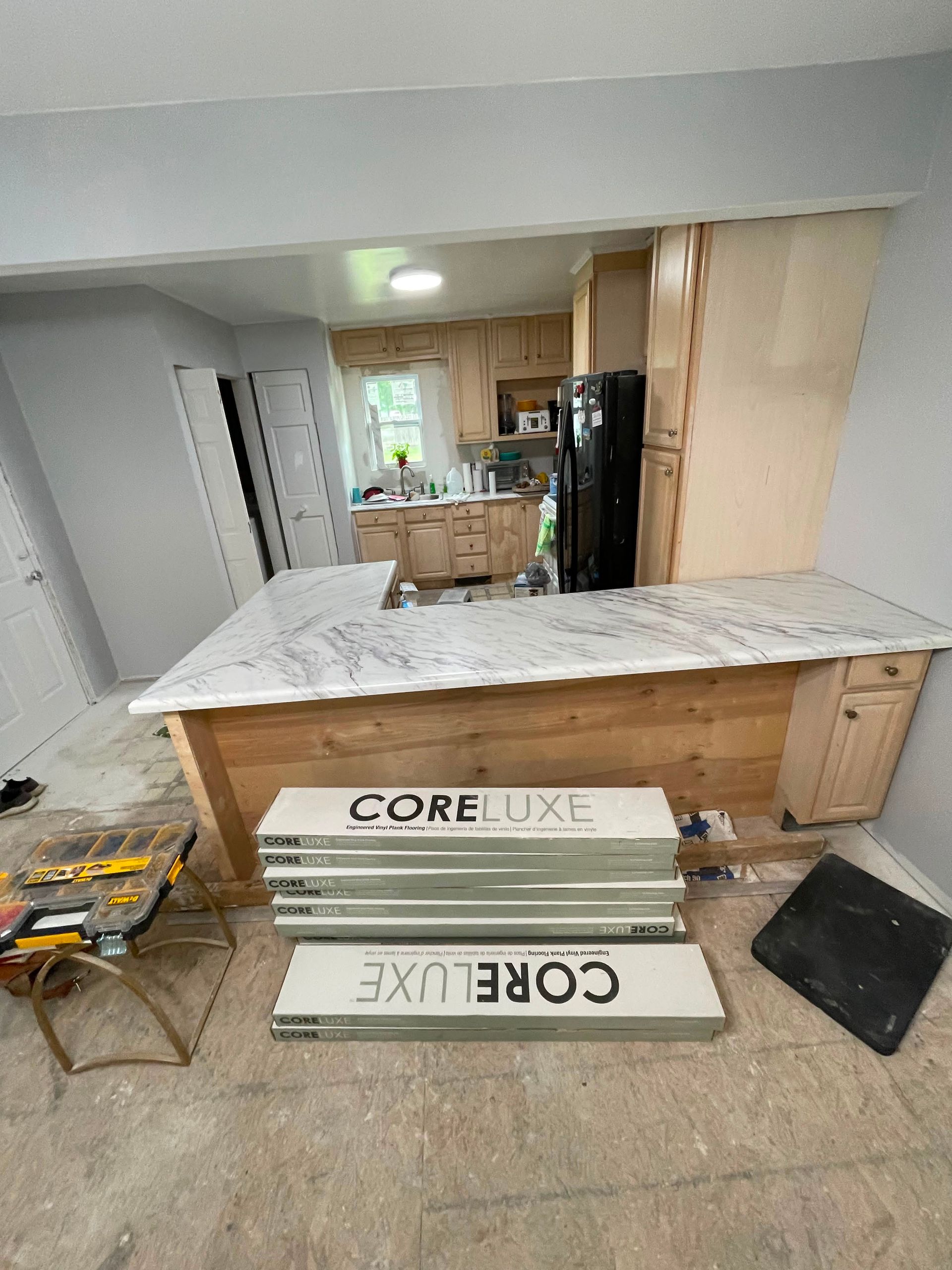 Kitchen under renovation with marble-topped island, cabinets, tools, and CORELUX boxes on the floor