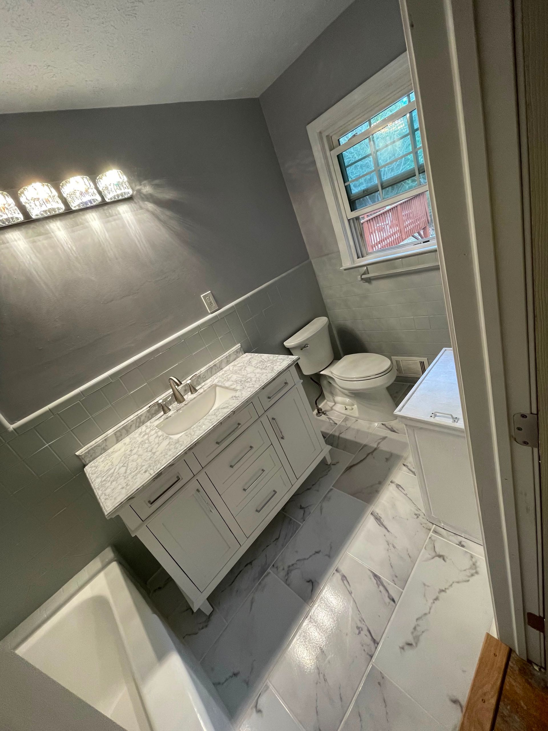 Gray bathroom with white vanity, toilet, window, and marble tile floor.