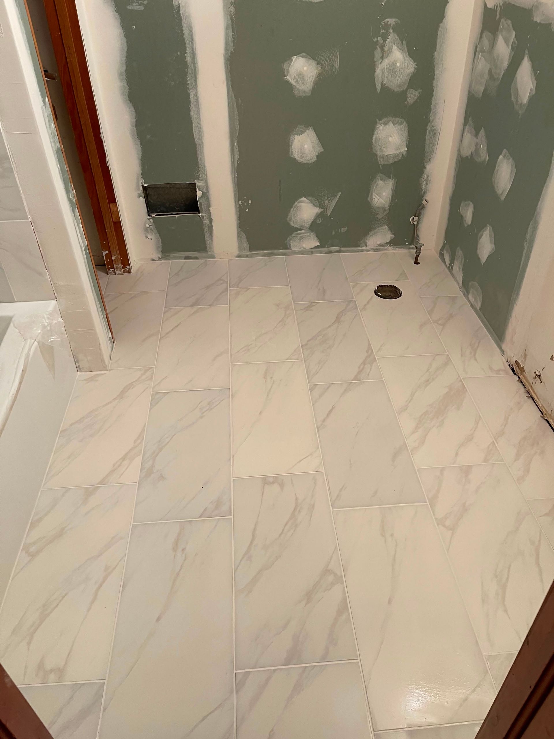 Partially renovated bathroom with white tile floor, unfinished green walls, and a shower drain