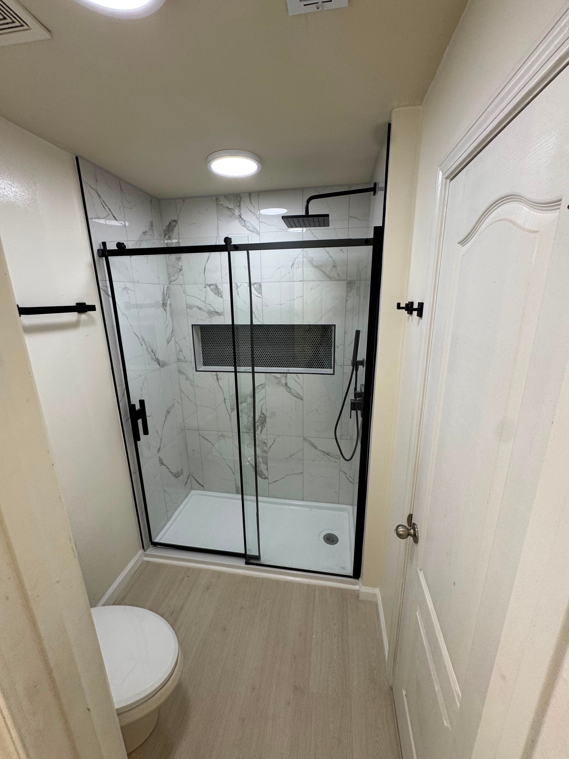 Small bathroom with a glass walk-in shower, toilet, and white door, viewed from the doorway.