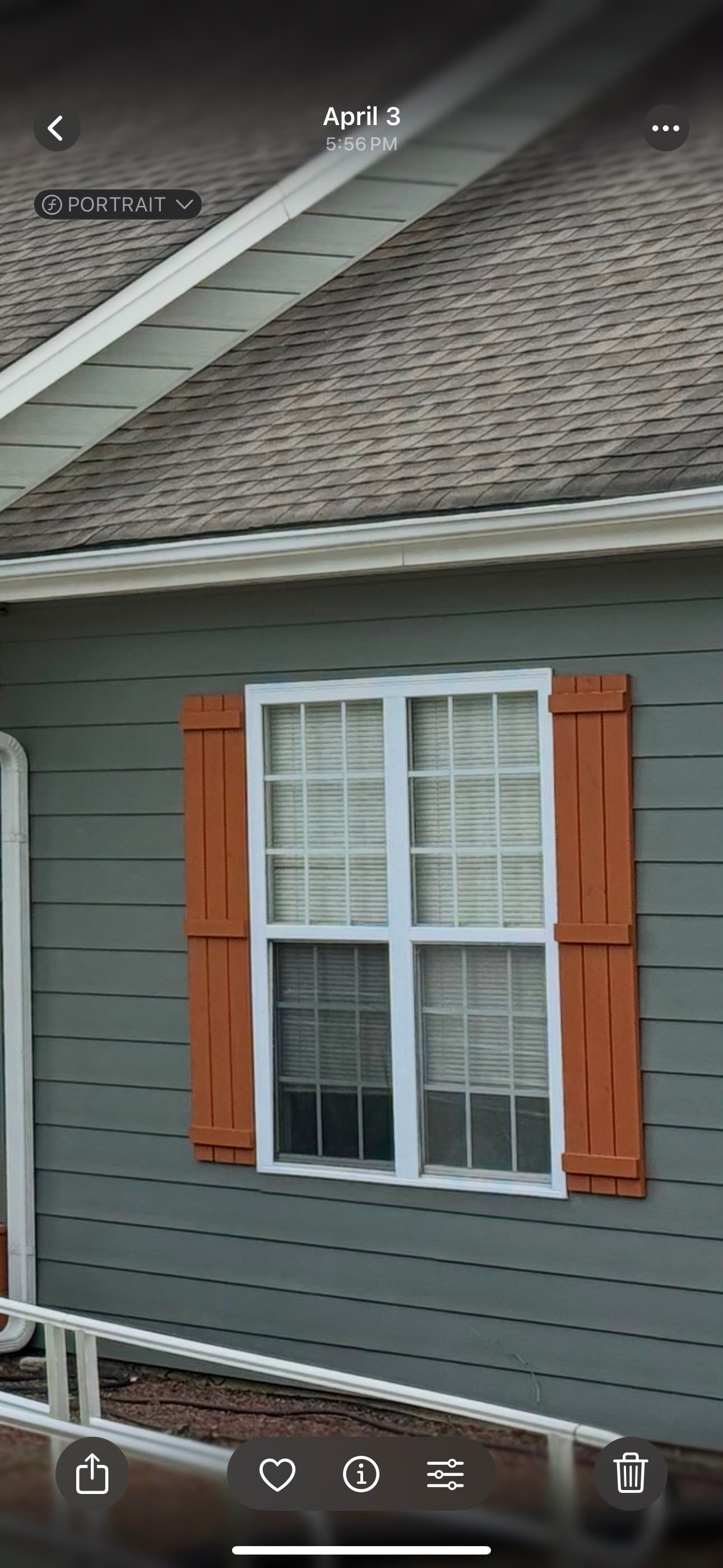 House window with orange shutters on gray siding under a shingled roof