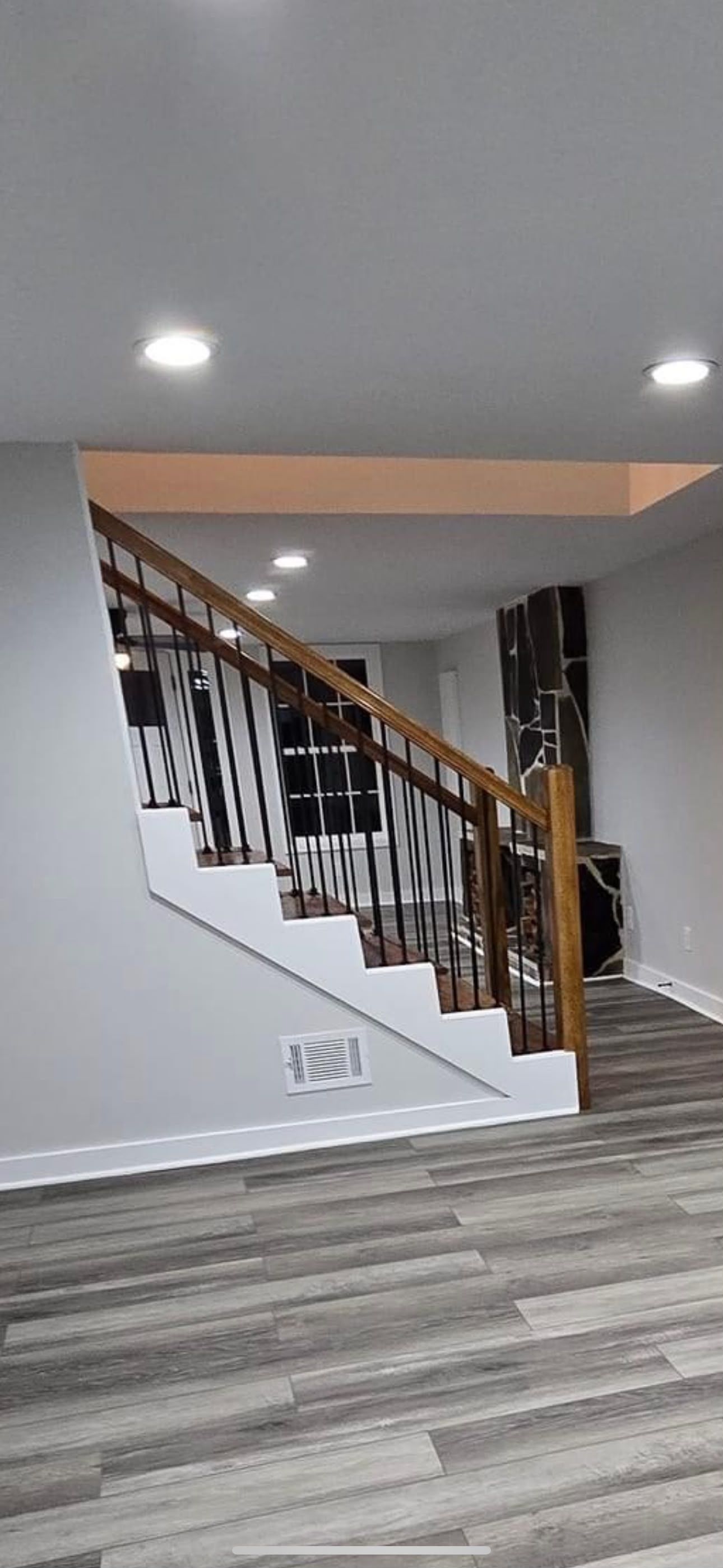 Empty stairwell in a home with white walls, wood railing, and gray striped flooring