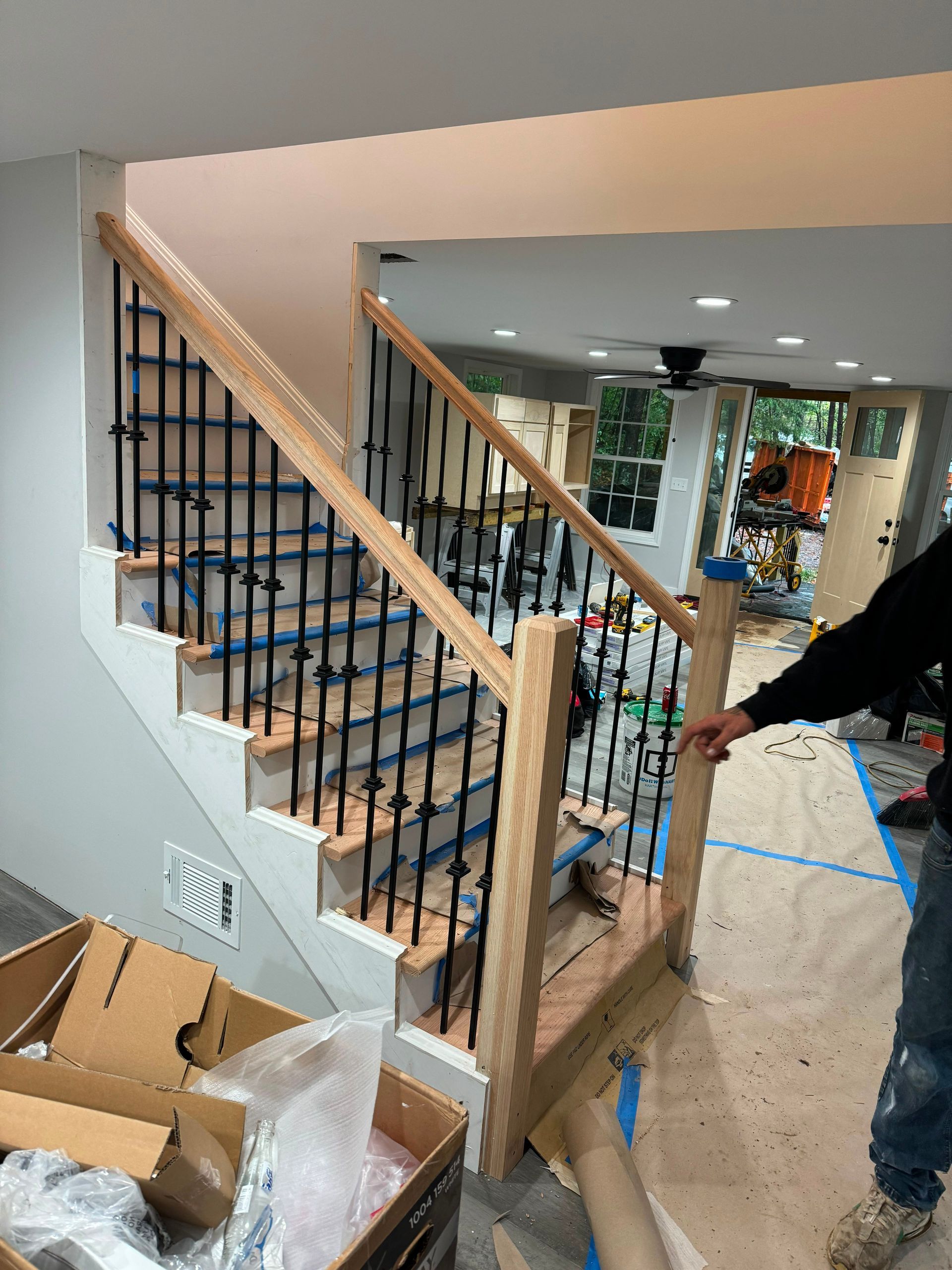 Staircase under construction with wood railings, blue tape, and cardboard boxes in a home interior