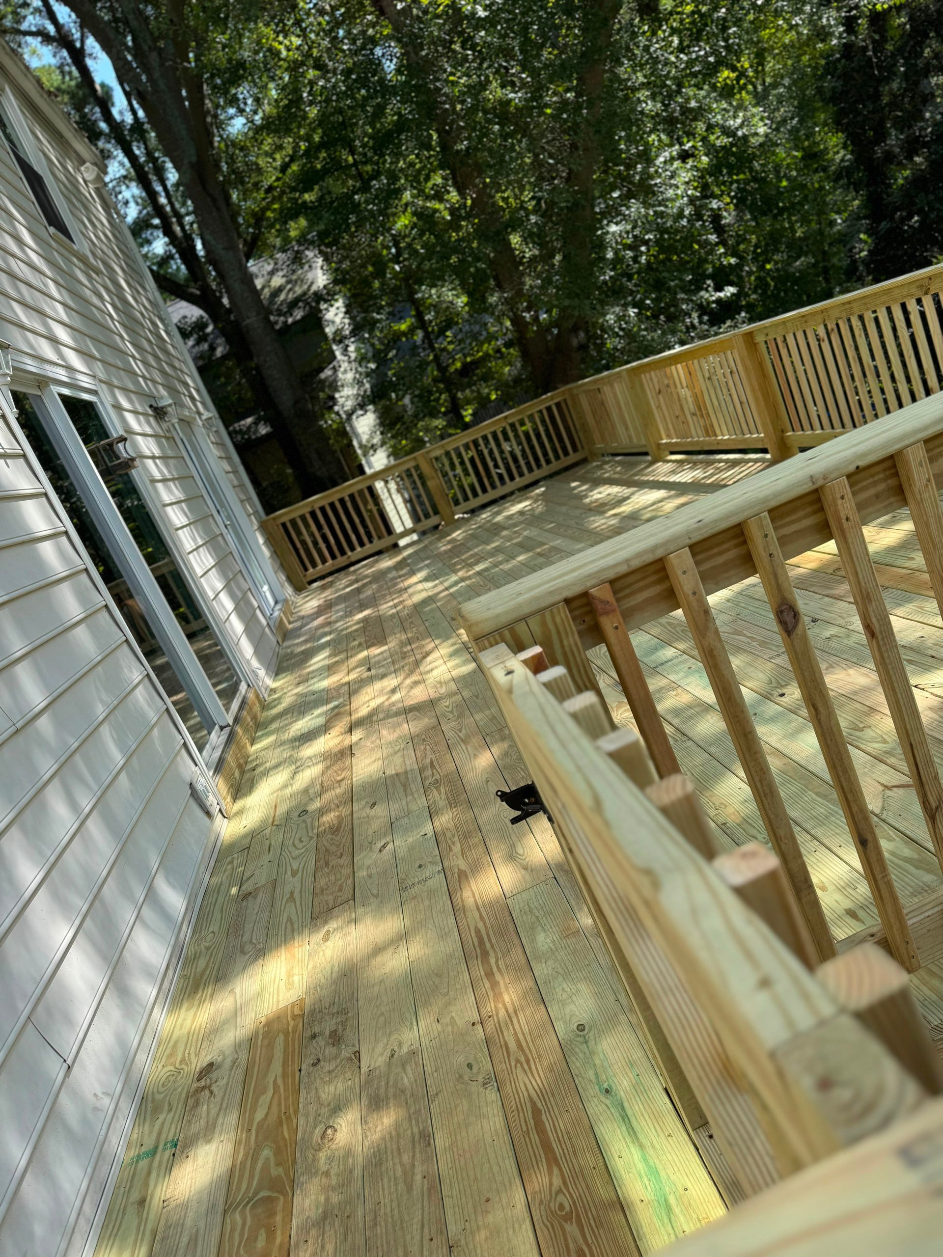 Wooden deck and ramp beside a white house, with railings and trees in the background.