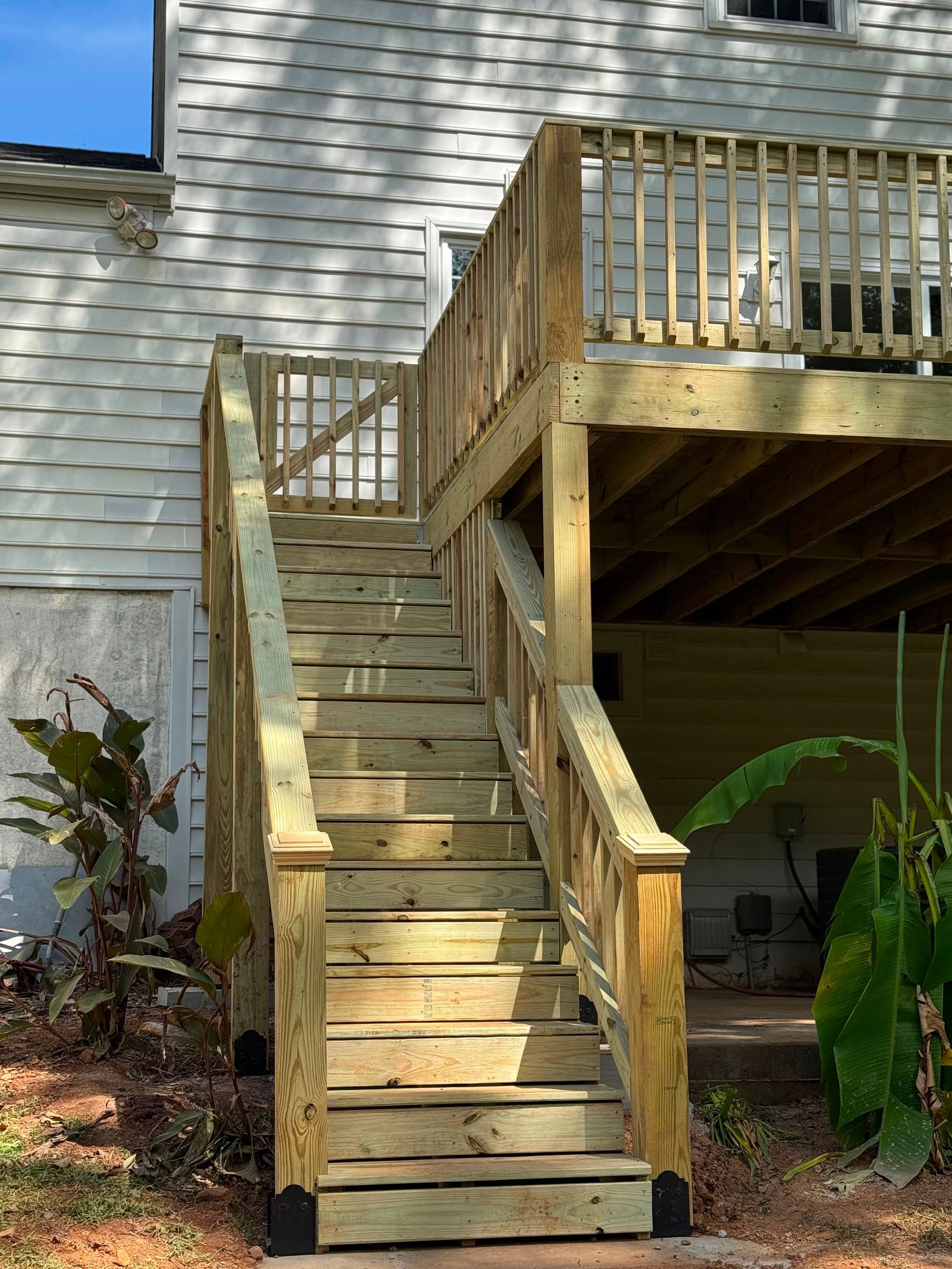 Wooden outdoor stairs with railings leading to a raised deck beside a white house.