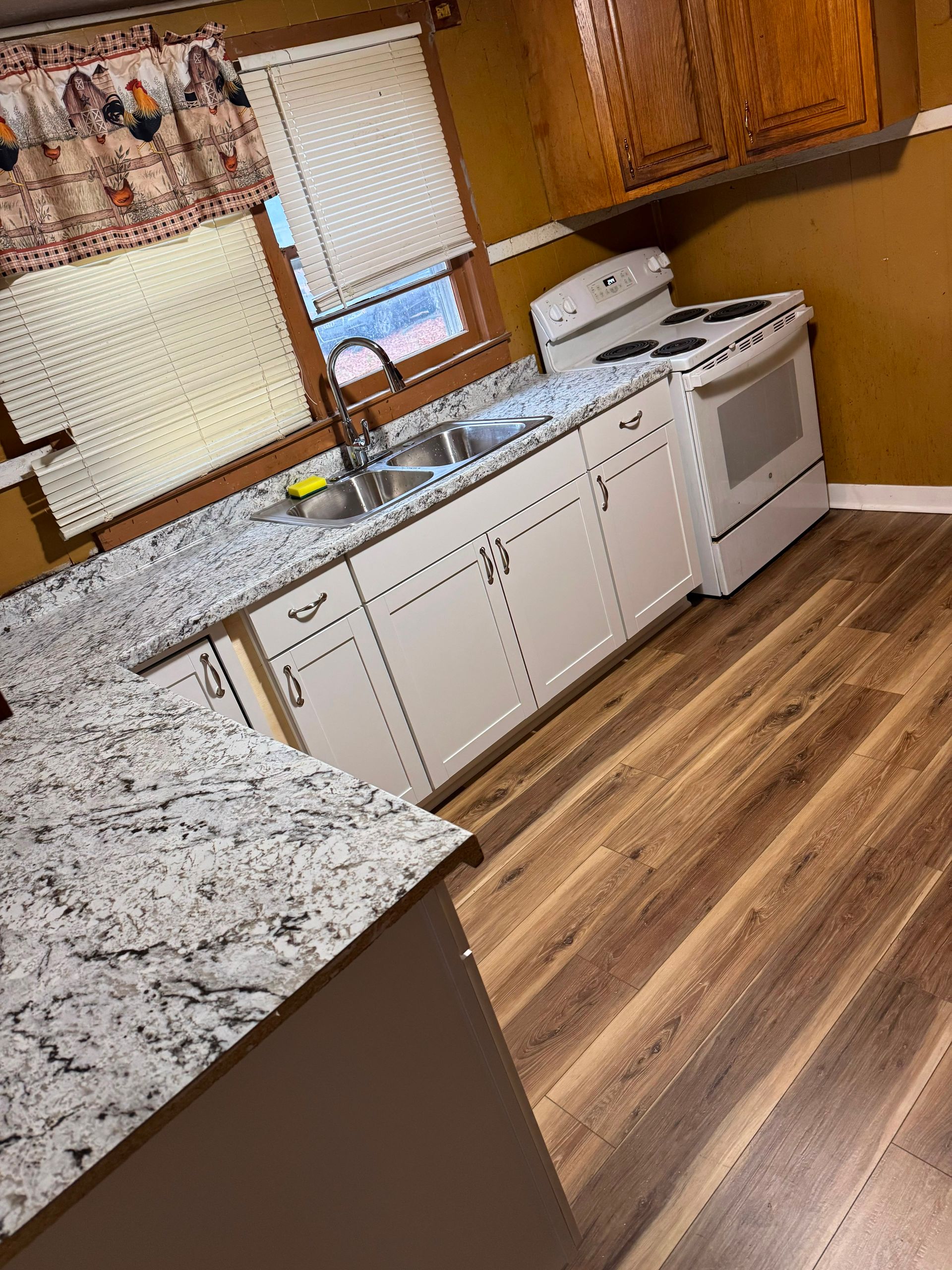 Bright kitchen with white cabinets, granite counters, wood floors, and a white stove by the window.