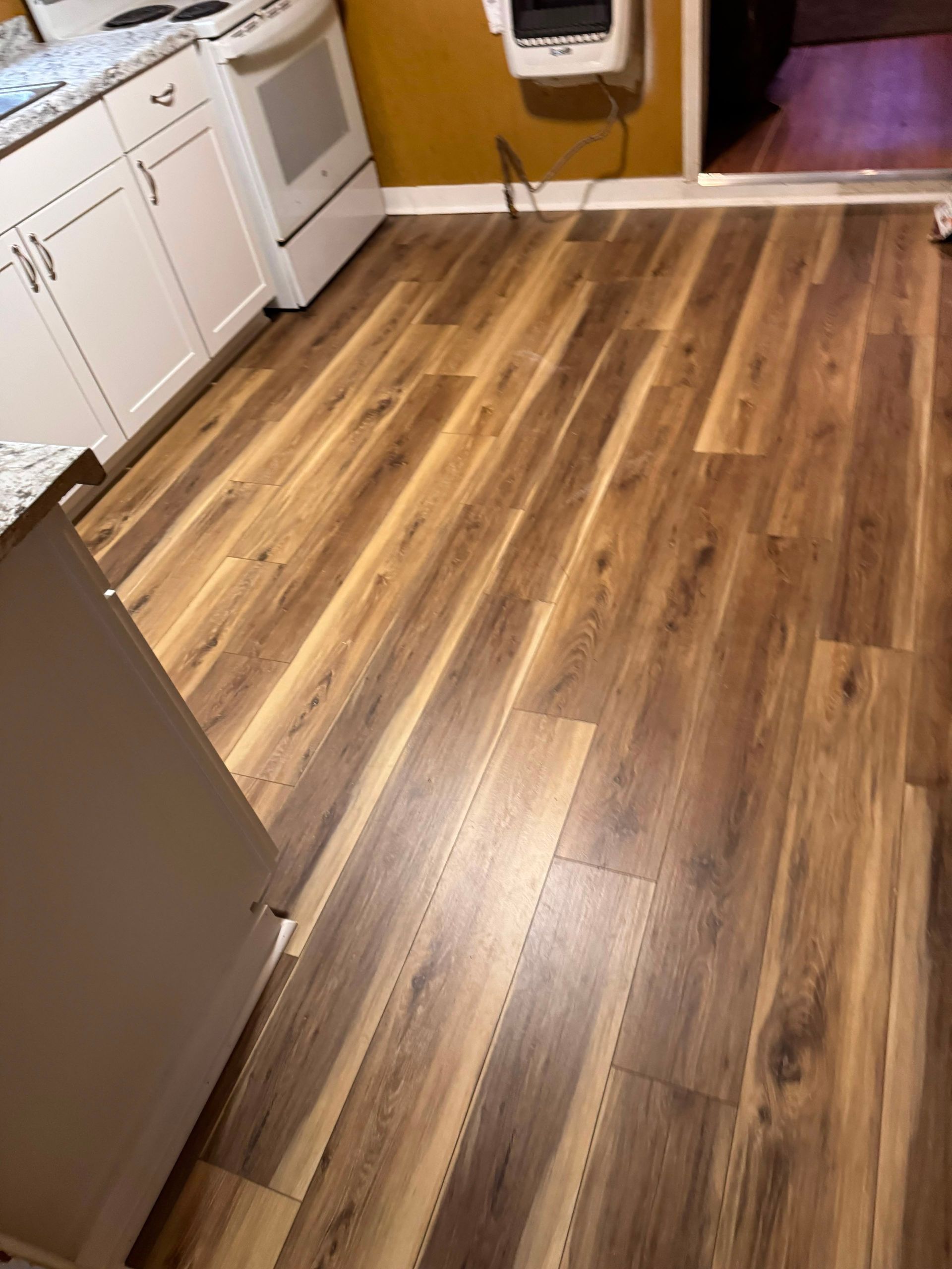 Wood-look laminate kitchen floor with white cabinets, stove, and a doorway in the background