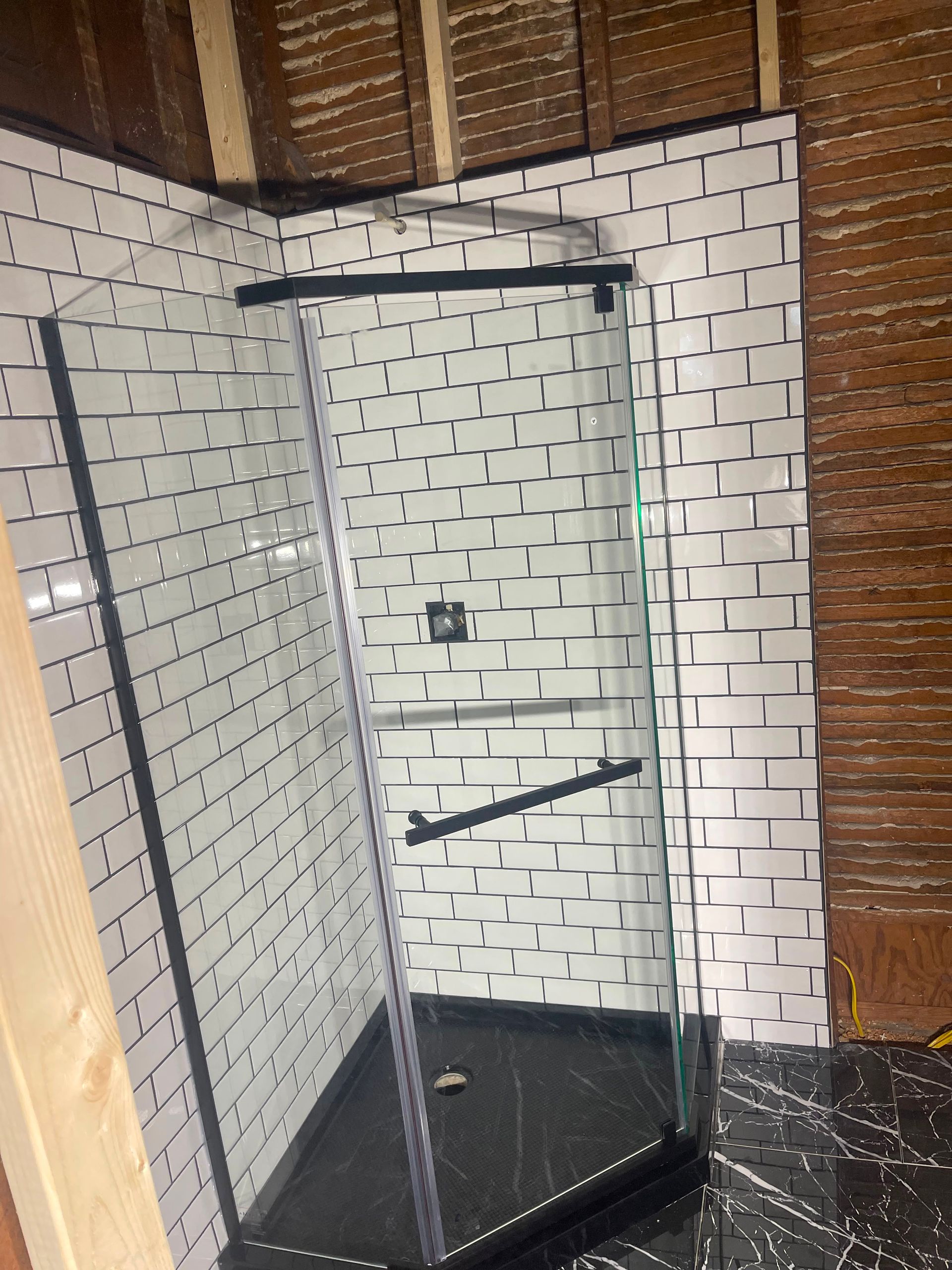 Glass shower enclosure in a bathroom with white brick-pattern tile walls and dark floor.